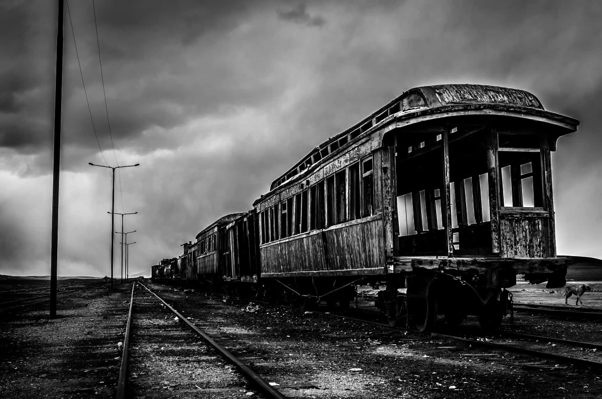  壁紙 — 一張令人難忘的黑白照片，拍攝了被遺棄的復古火車車廂在空曠的軌道上生鏽，背景是暴風雨的天空。