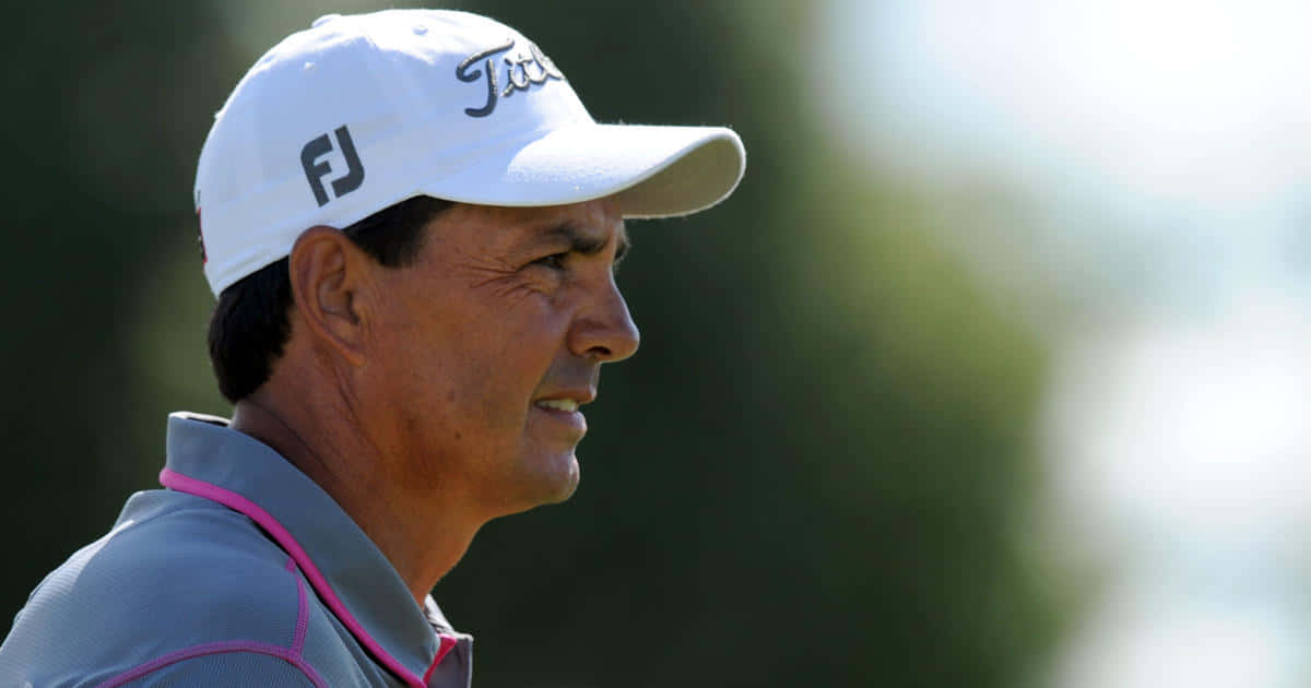 壁紙 — 一位專注的高爾夫球手，戴著白色 Titleist 帽子，穿著灰色帶粉紅邊的襯衫，在陽光明媚的球場上專注地向前看。