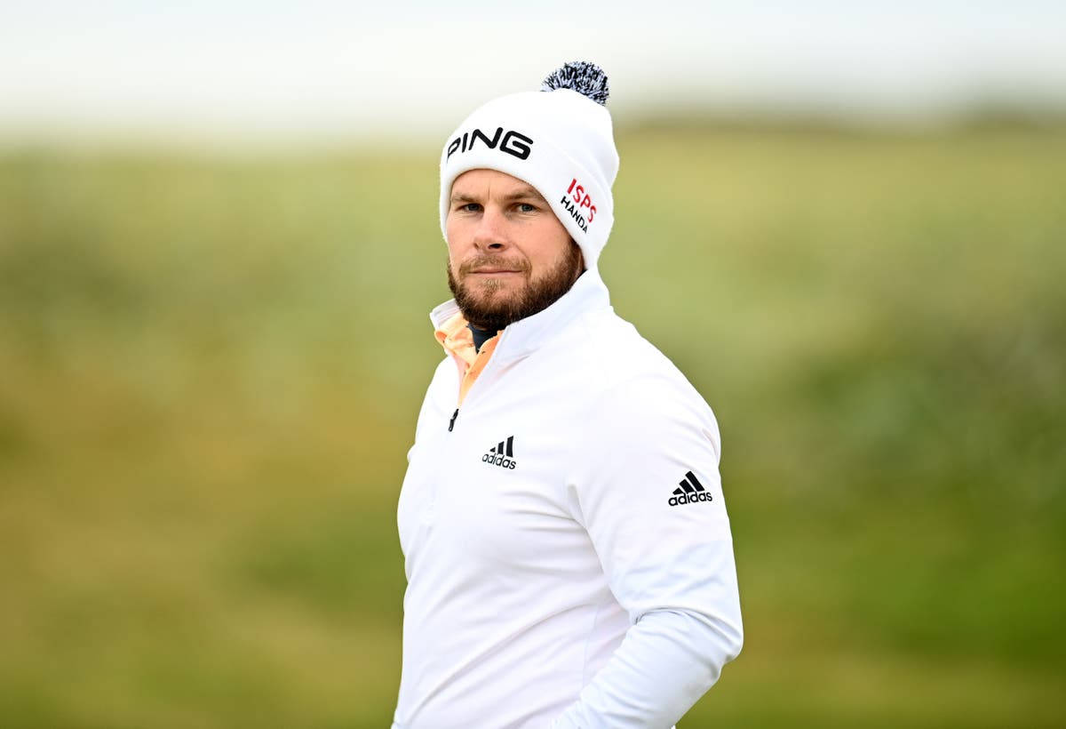 Tyrrell Hatton 桌布 壁紙 — 一位專注的高爾夫球手戴著白色冷帽和外套，站在有模糊自然背景的草地上。