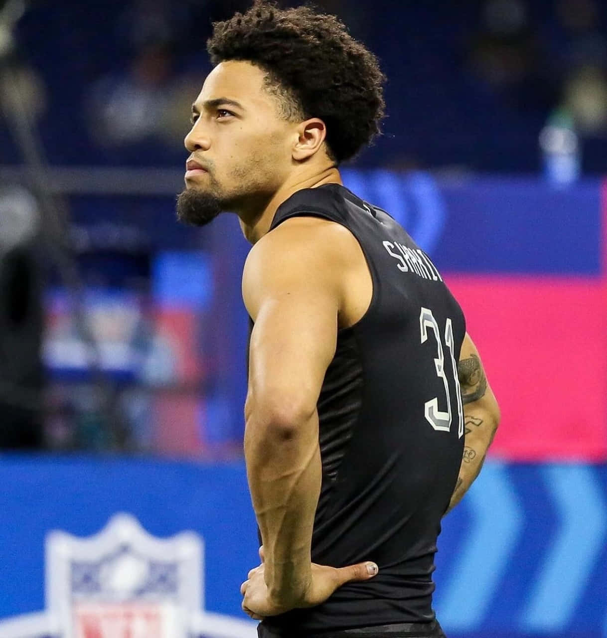  壁紙 — 一位專注的NFL球員身穿黑色球衣，號碼31，雙手叉腰站在明亮的燈光下的球場上。