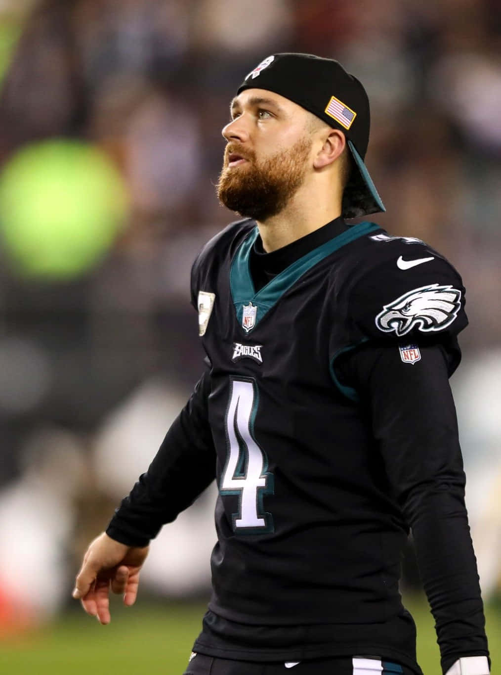  壁紙 — 一位專注的NFL四分衛穿著黑色Eagles球衣，號碼4，在夜間比賽中於球場燈光下向上看。