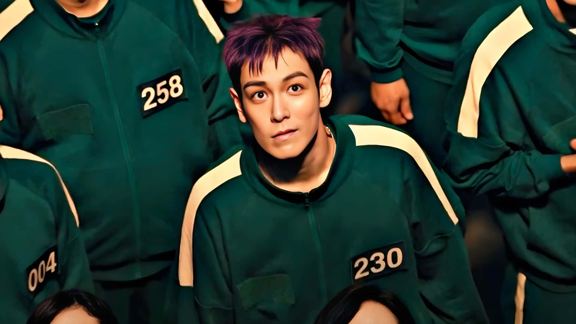  壁紙 — 一名紫髮年輕男子身穿綠色有號碼的運動服，被其他穿著相同制服的人包圍，專注地向前凝視。