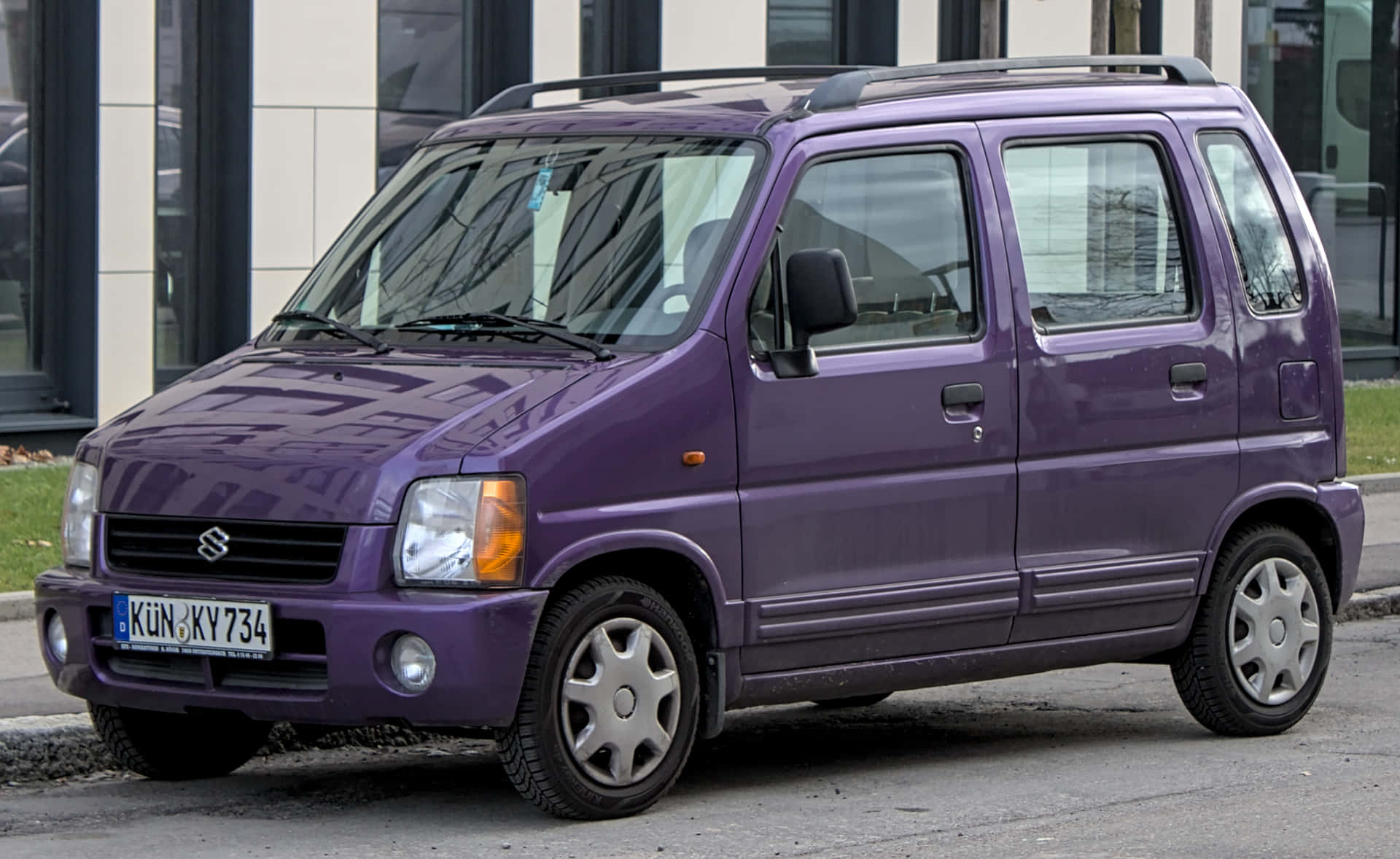  壁紙 — 一輛充滿活力的紫色鈴木Every小型貨車停泊在城巿街道上，背景是現代建築。