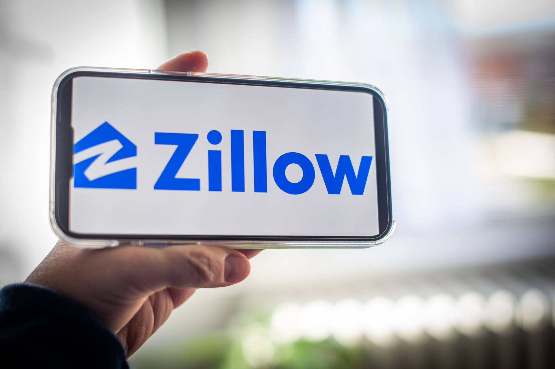 手拿著顯示 Zillow 房地產應用程式標誌的手機