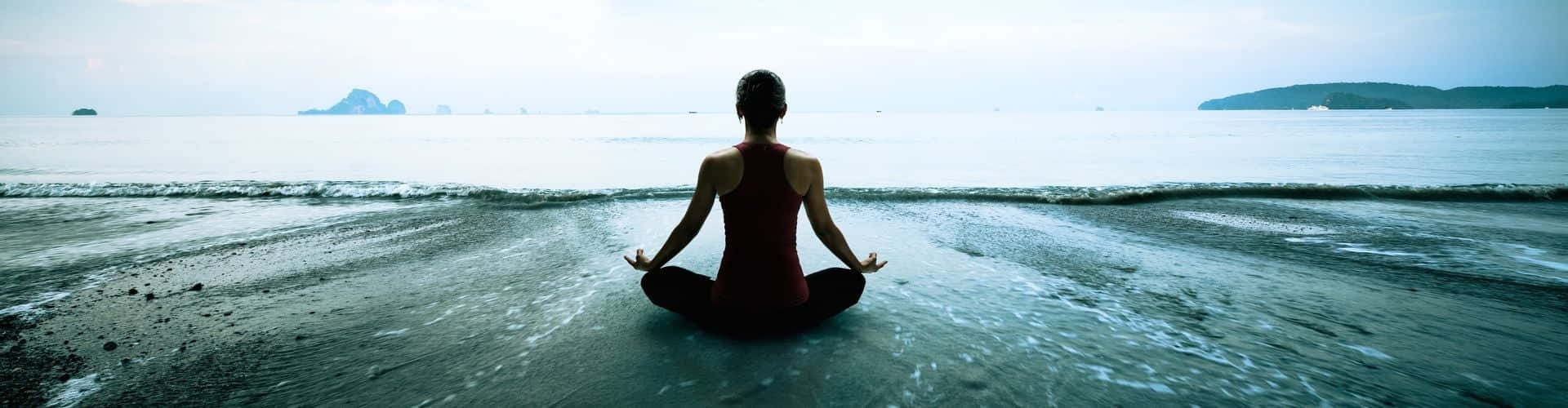 Transcendental 桌布 壁紙 — 一人在濕漉漉的沙灘上以蓮花坐姿冥想，柔和的海浪在朦朧的天空下翻滾。