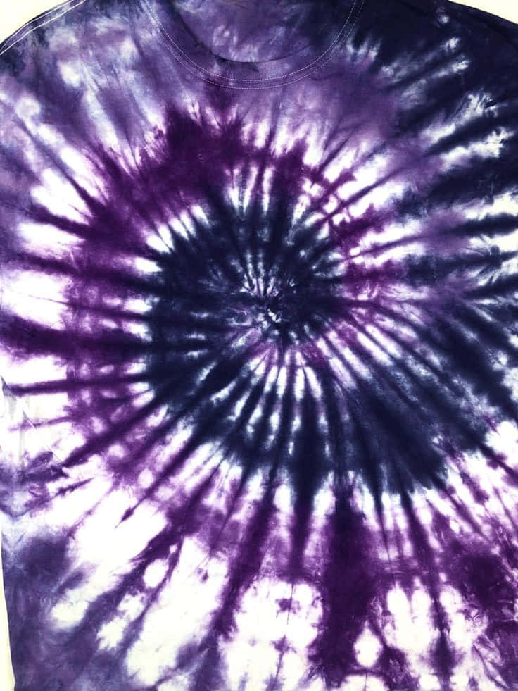 Purple Dye 桌布 壁紙 — 一件T恤的近距離特寫，帶有從中心放射出的鮮豔紫色和白色螺旋紮染圖案。