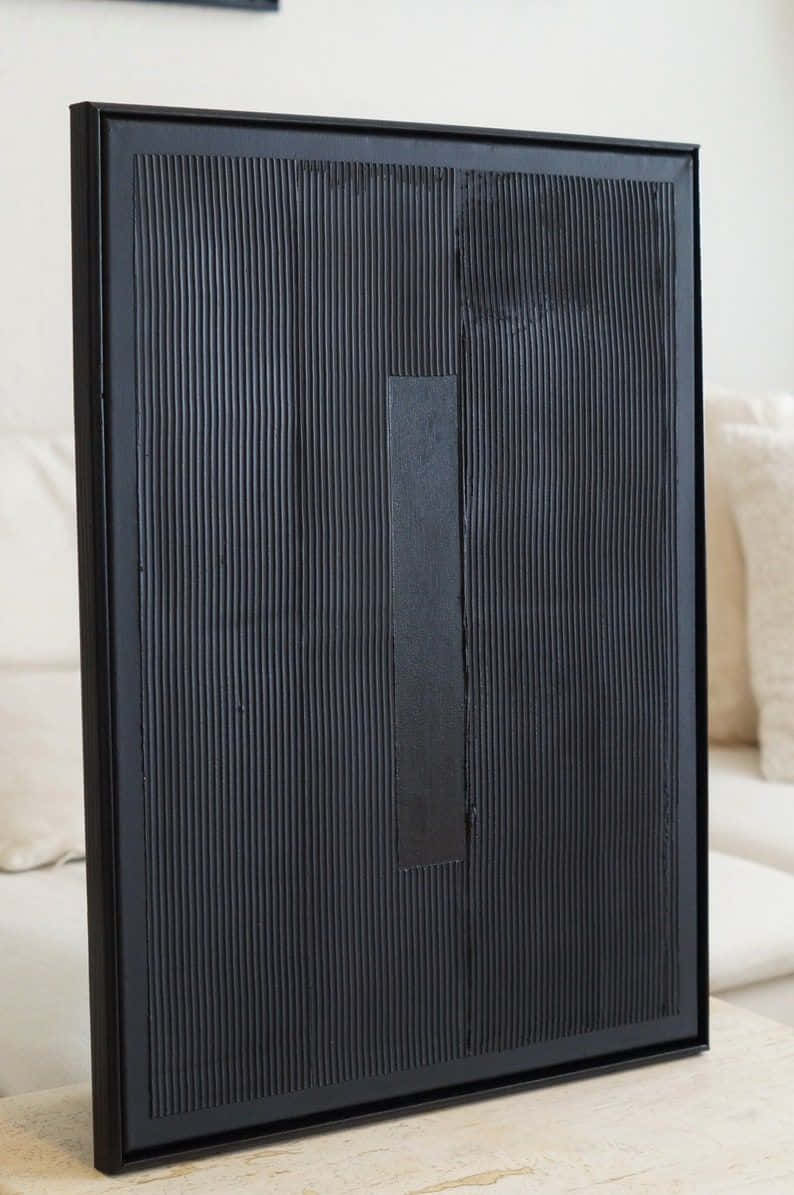Modern Minimalist Art 桌布 壁紙 — 一件極簡風格的黑色紋理牆藝品，帶有垂直脊線和中央矩形空洞，立於淺色木質表面上。