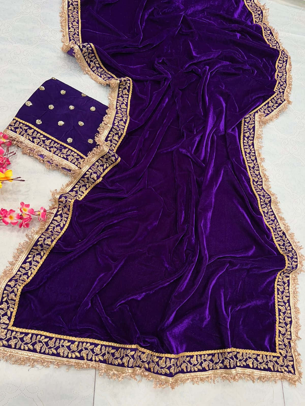 Purple Velvet 桌布 壁紙 — 一件華麗的紫色天鵝絨服飾，飾有金色刺繡和流蘇，披在淺色表面上，旁邊擺放著色彩繽紛的花朵。