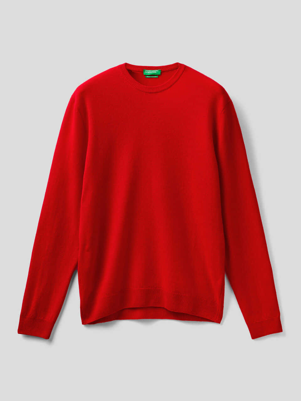 Red Sweater 桌布 壁紙 — 一件鮮紅色圓領毛衣，帶有綠色標籤，平放在中性灰色背景上。