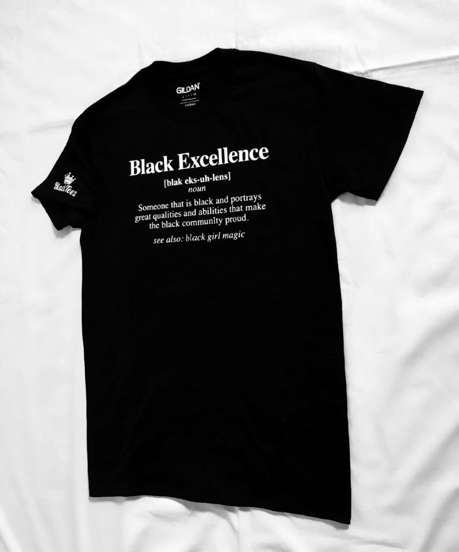 Black Excellence 桌布 壁紙 — 一件黑色T恤，上面有白色文字定義「Black Excellence」，平放在皺巴巴的白色布料表面上。