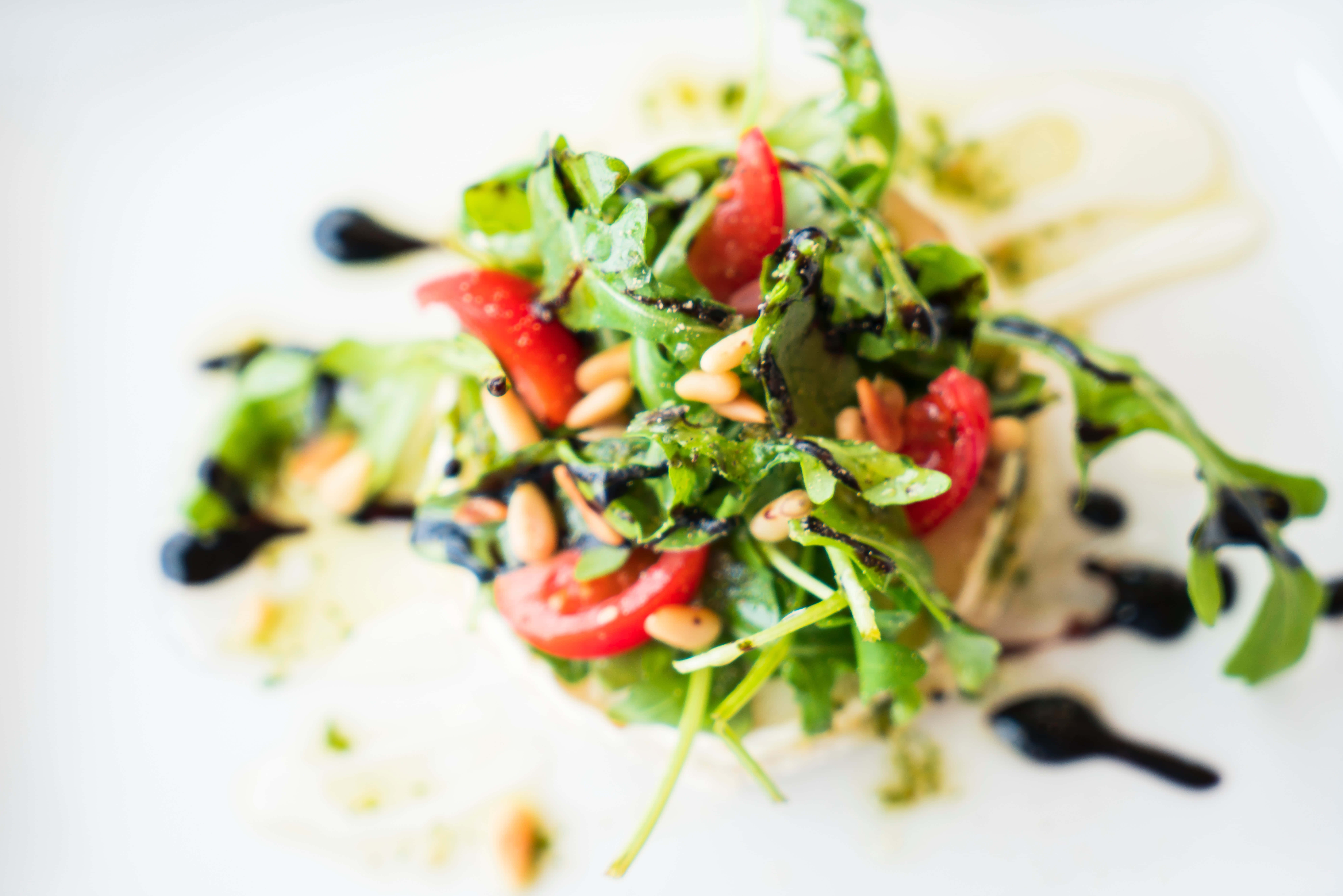 沙律 桌布 壁紙 — 一份充滿活力的火箭菜沙律，配以車厘番茄、松子仁和黑醋汁，精緻地擺放在白色碟上。