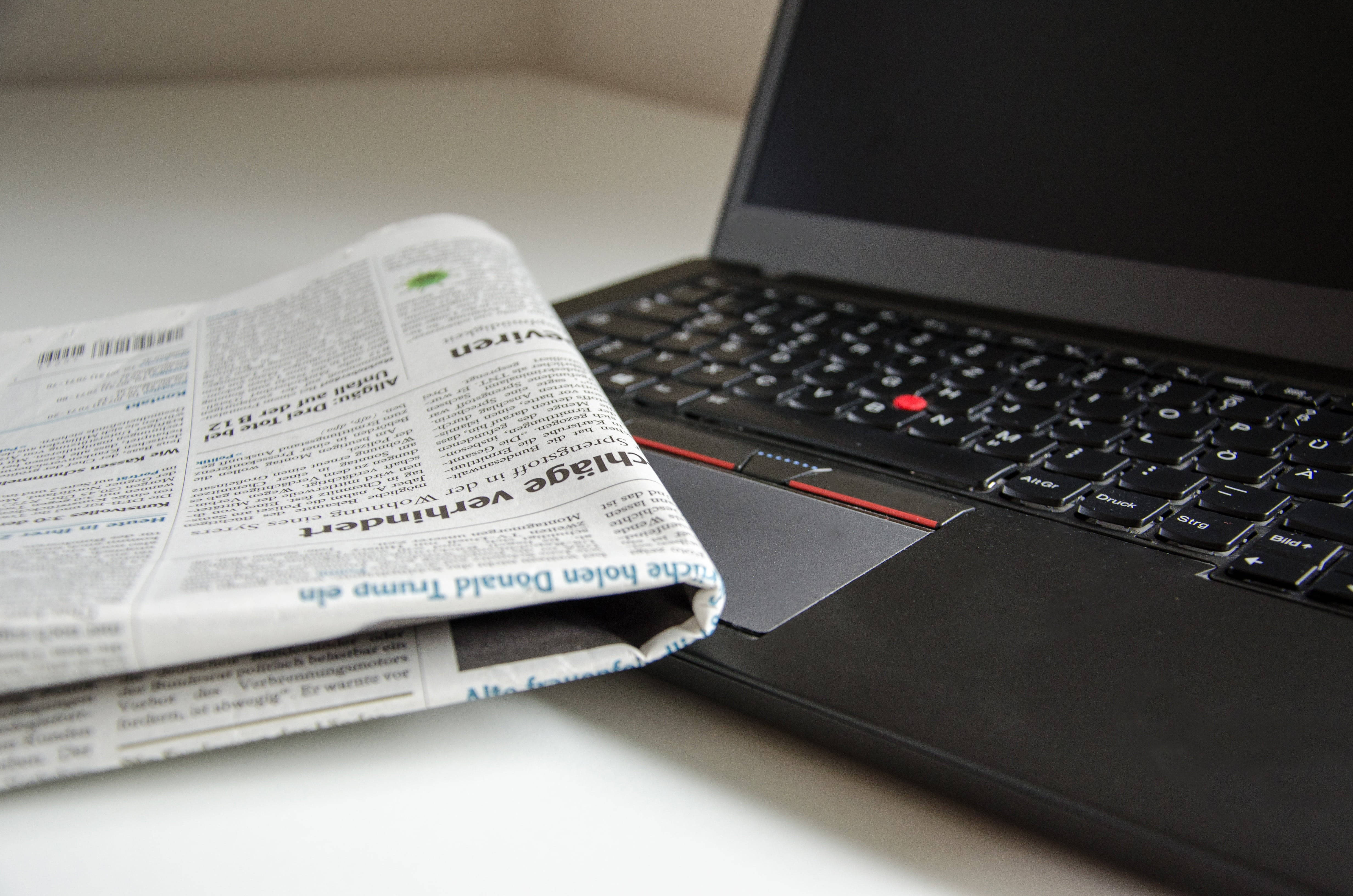 Newspaper 桌布 壁紙 — 一份摺疊的報紙放在現代工作空間的白色桌子上，旁邊是一部黑色手提電腦。