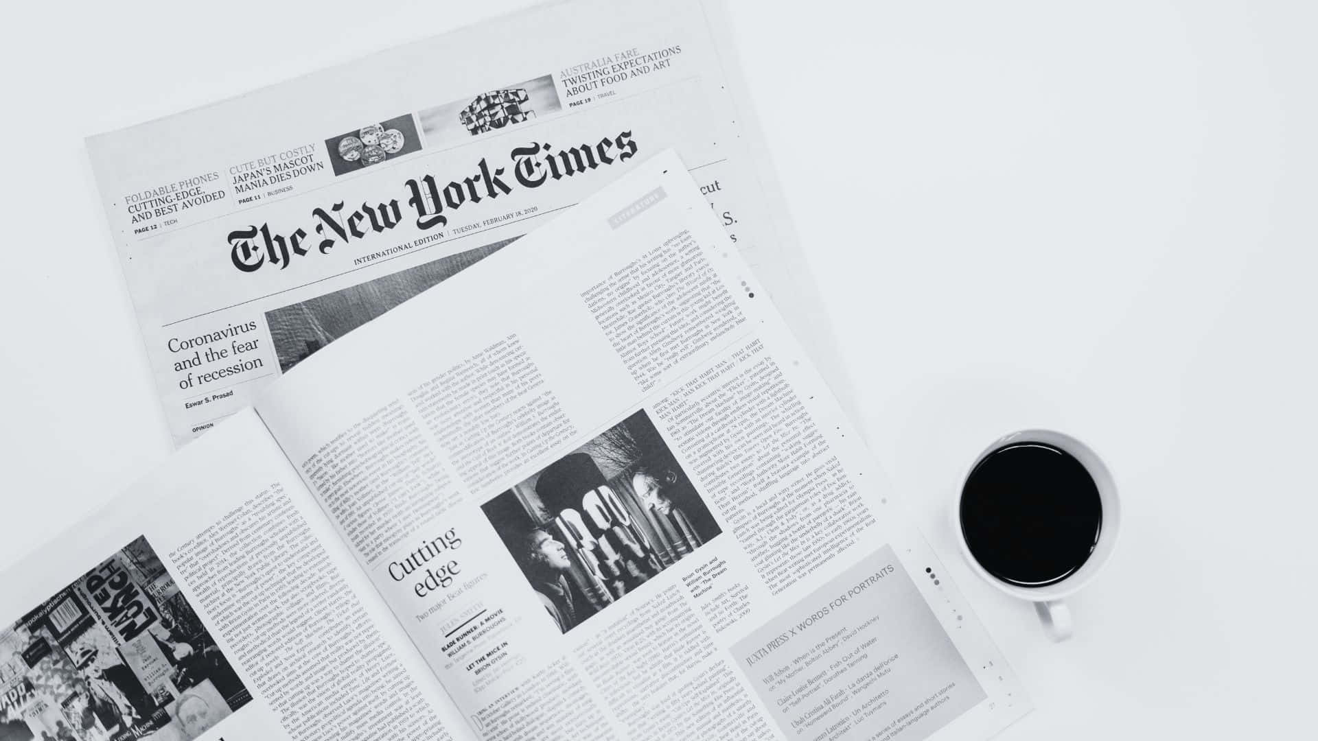 Black And White Newspaper 桌布 壁紙 — 一份黑白風格的《紐約時報》報紙攤開，旁邊放著一個白色咖啡杯，置於潔白的表面上。