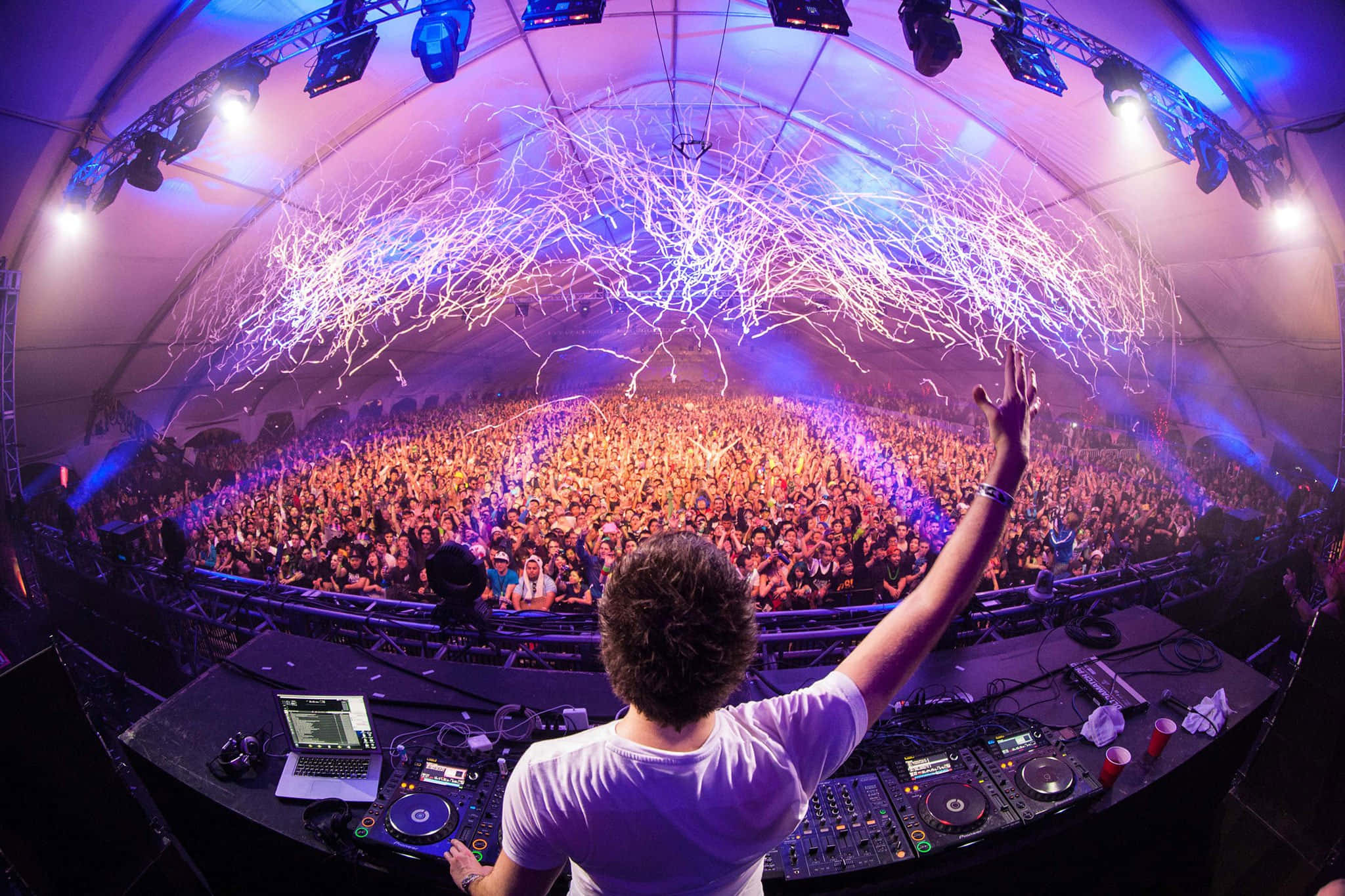 Electronic Dance Music 桌布 壁紙 — 一位DJ在電光藍色燈光和閃爍激光束的穹頂下，面向龐大的人群舉起一隻手臂。