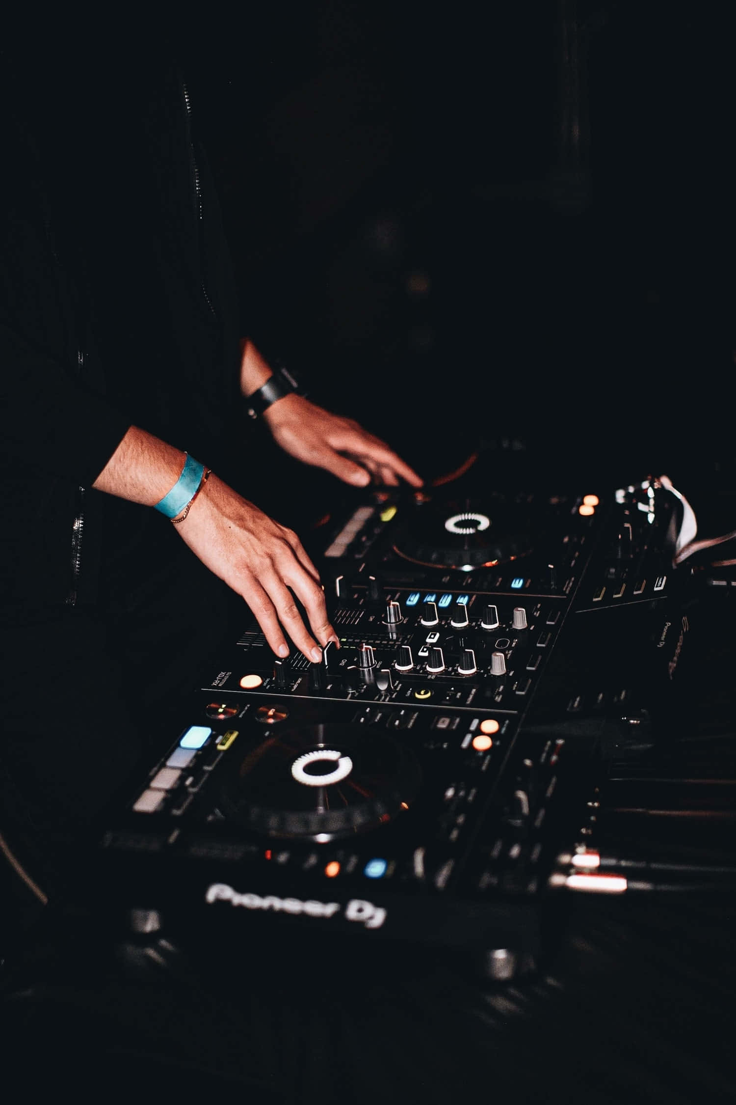 DJ 桌布 壁紙 — 一位DJ的手在昏暗的舞台燈光下熟練地操控著先鋒DJ混音器上發光的控制裝置。