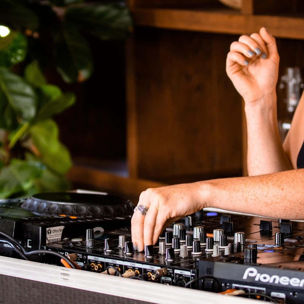 DJ 桌布 壁紙 — 一位DJ的手熟練地調整先鋒混音器上的旋鈕，背景有綠色植物和木架。