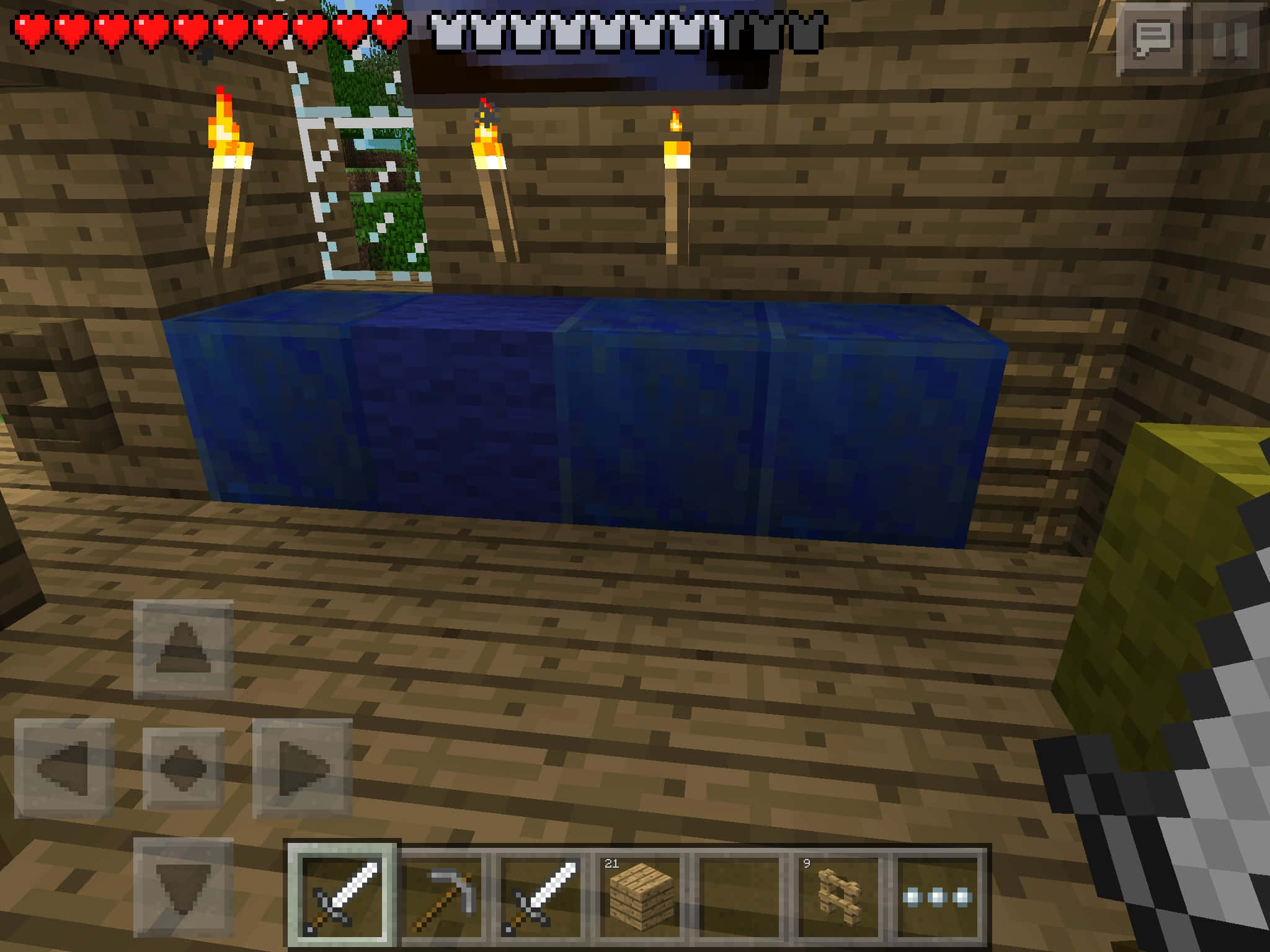 Minecraft Pocket Edition 桌布 壁紙 — 一位Minecraft玩家站在木製地下房間，火炬照亮藍色水方塊和合成台。