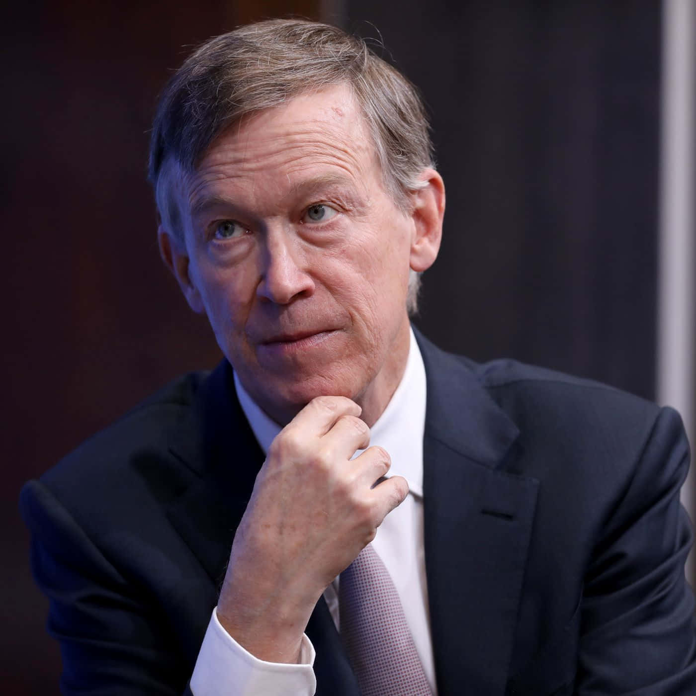 John Hickenlooper - The Thoughtful Politician 壁紙 — 一位中年男士的近距離肖像，身穿深色西裝和圖案領帶，手托下巴，表情若有所思。