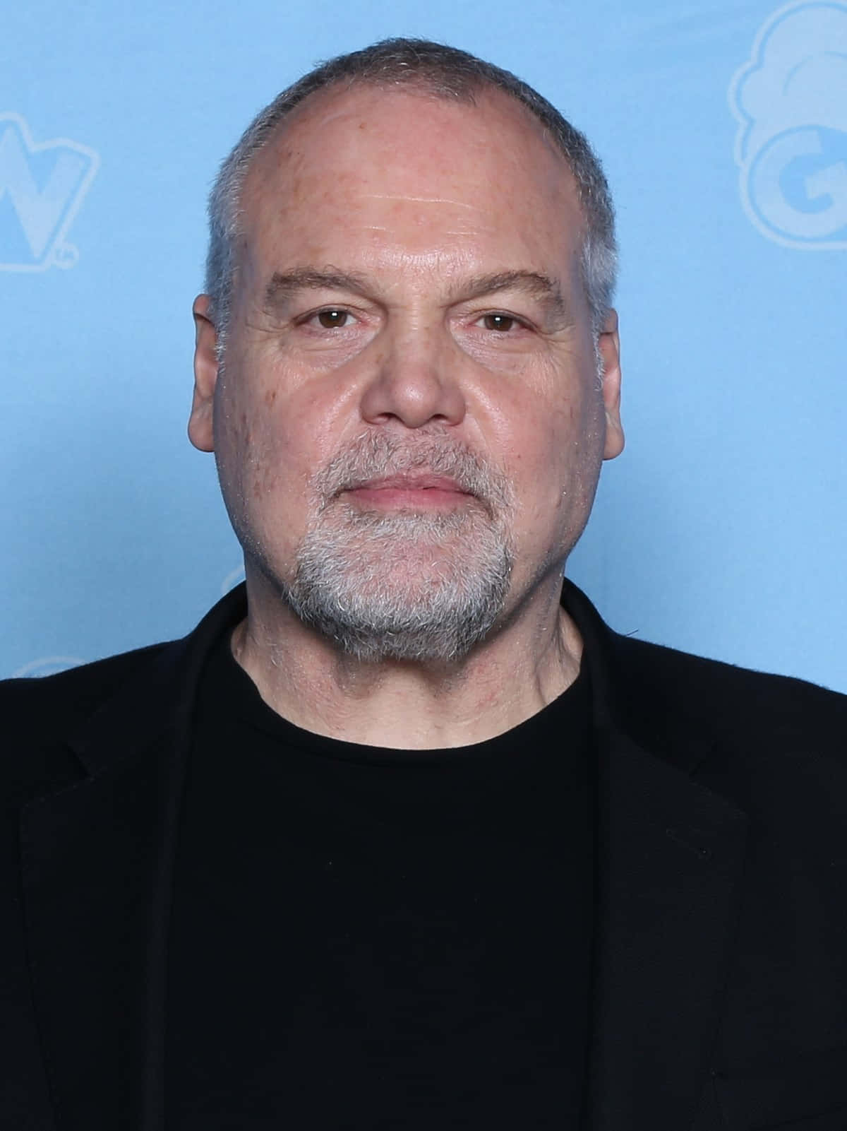 Vincent D'onofrio 桌布 壁紙 — 一位中年男子嘅近距離肖像，佢有灰白頭髮同鬍鬚，著住黑色西裝，背景係淺藍色。