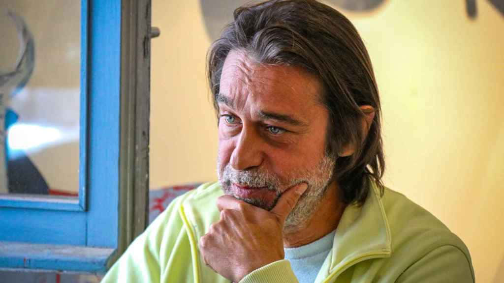 Jordi Mollà 桌布 壁紙 — 一位中年男子帶著沉思的表情，在藍色窗框的窗戶旁用手托著下巴。