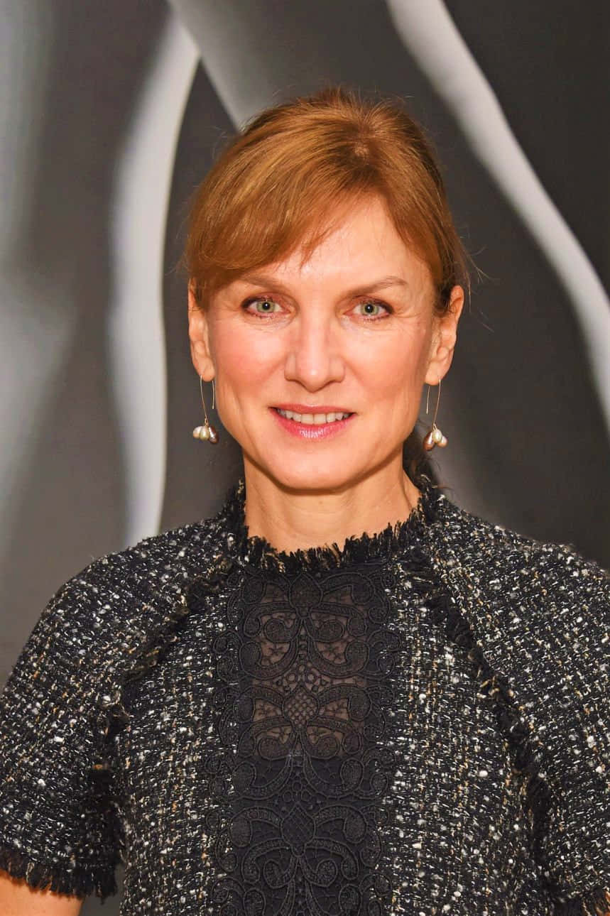 Fiona Bruce 桌布 壁紙 — 一位優雅的女士，紅褐色頭髮，穿著質感黑色蕾絲和閃亮外套，在現代抽象灰色和白色背景前溫暖微笑。