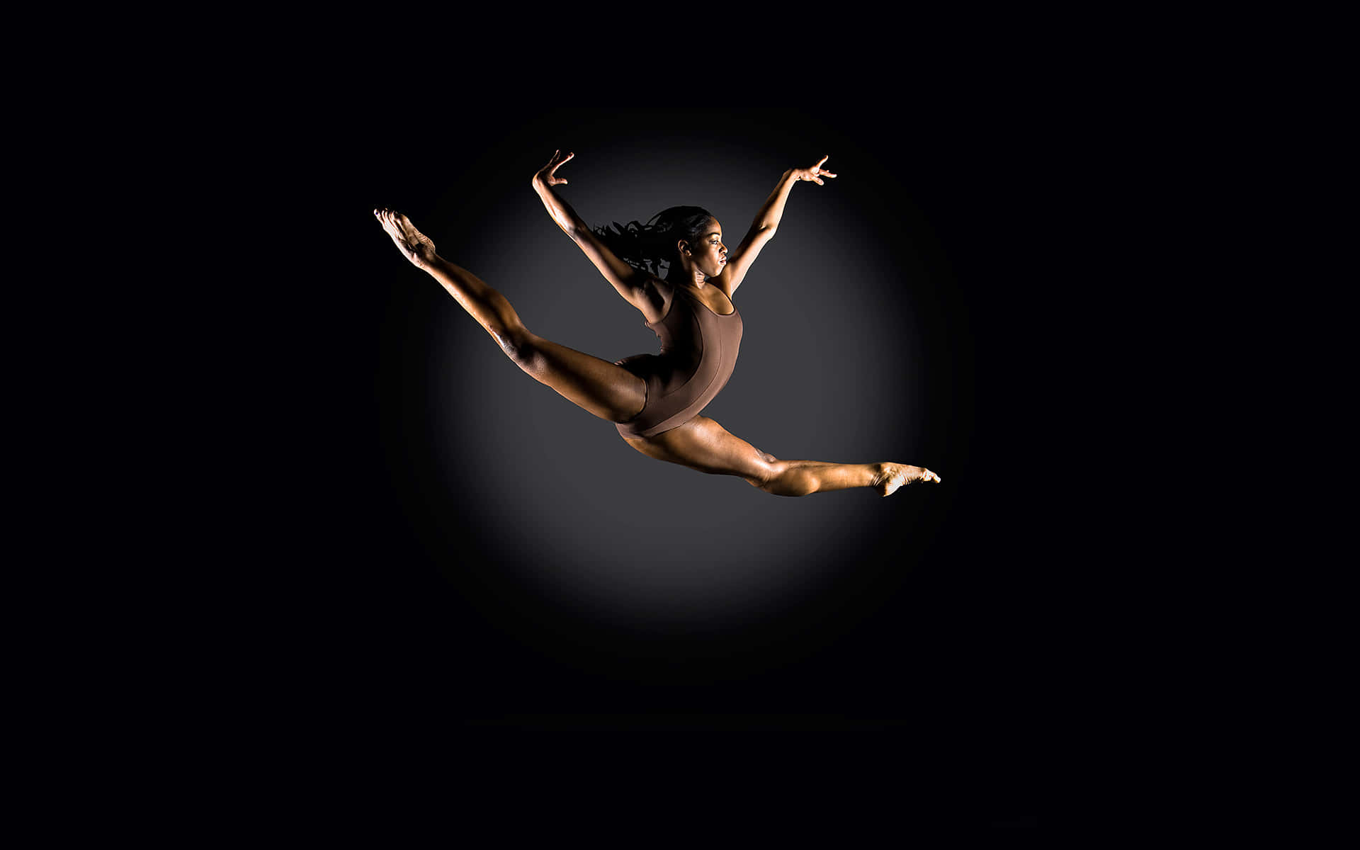 Gymnastics 桌布 壁紙 — 一位優雅的舞者在純黑背景和柔和聚光燈下，以戲劇性的姿勢騰空躍起。