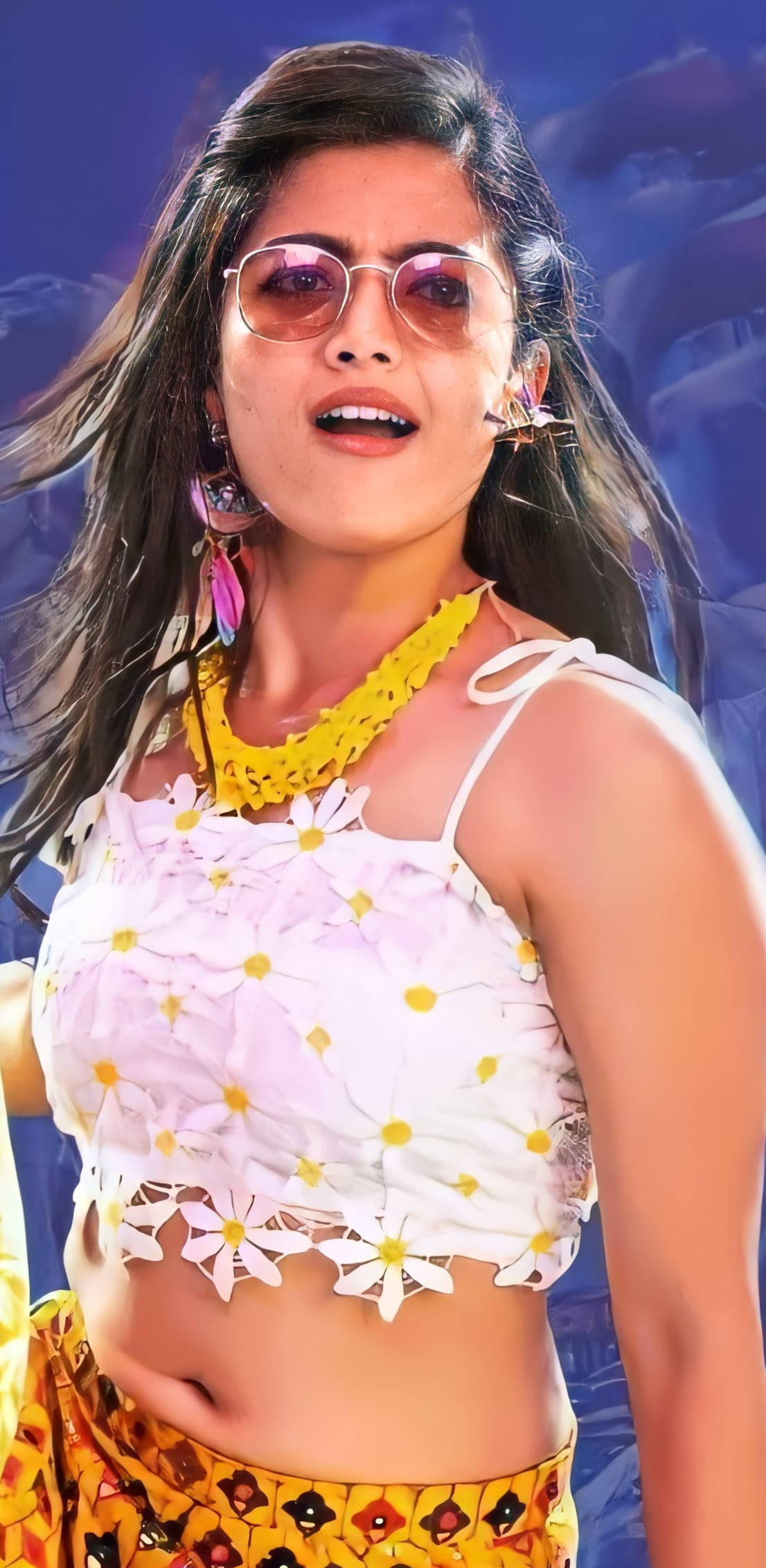 telugu 桌布 壁紙 — 一位充滿活力的女性，長長的黑髮，戴著粉紅色太陽眼鏡，穿著花卉短上衣和黃色圖案裙子，背景是夢幻的藍天。
