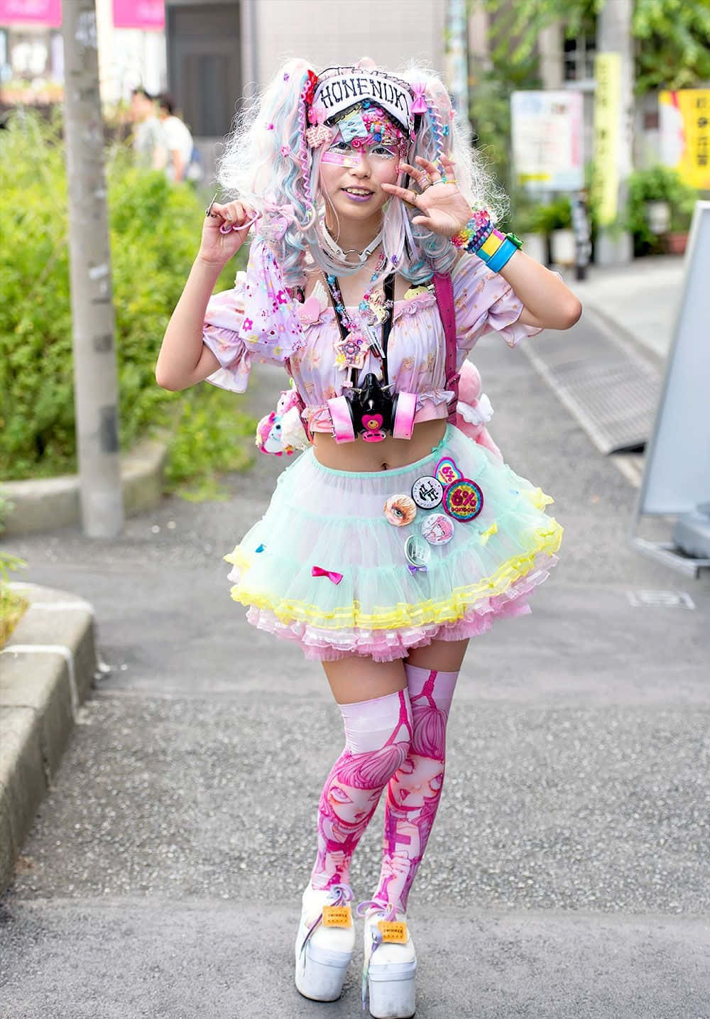Harajuku Fashion 桌布 壁紙 — 一位充滿活力的街頭表演者穿著色彩繽紛的原宿風格服裝，在城市人行道上擺出和平手勢。