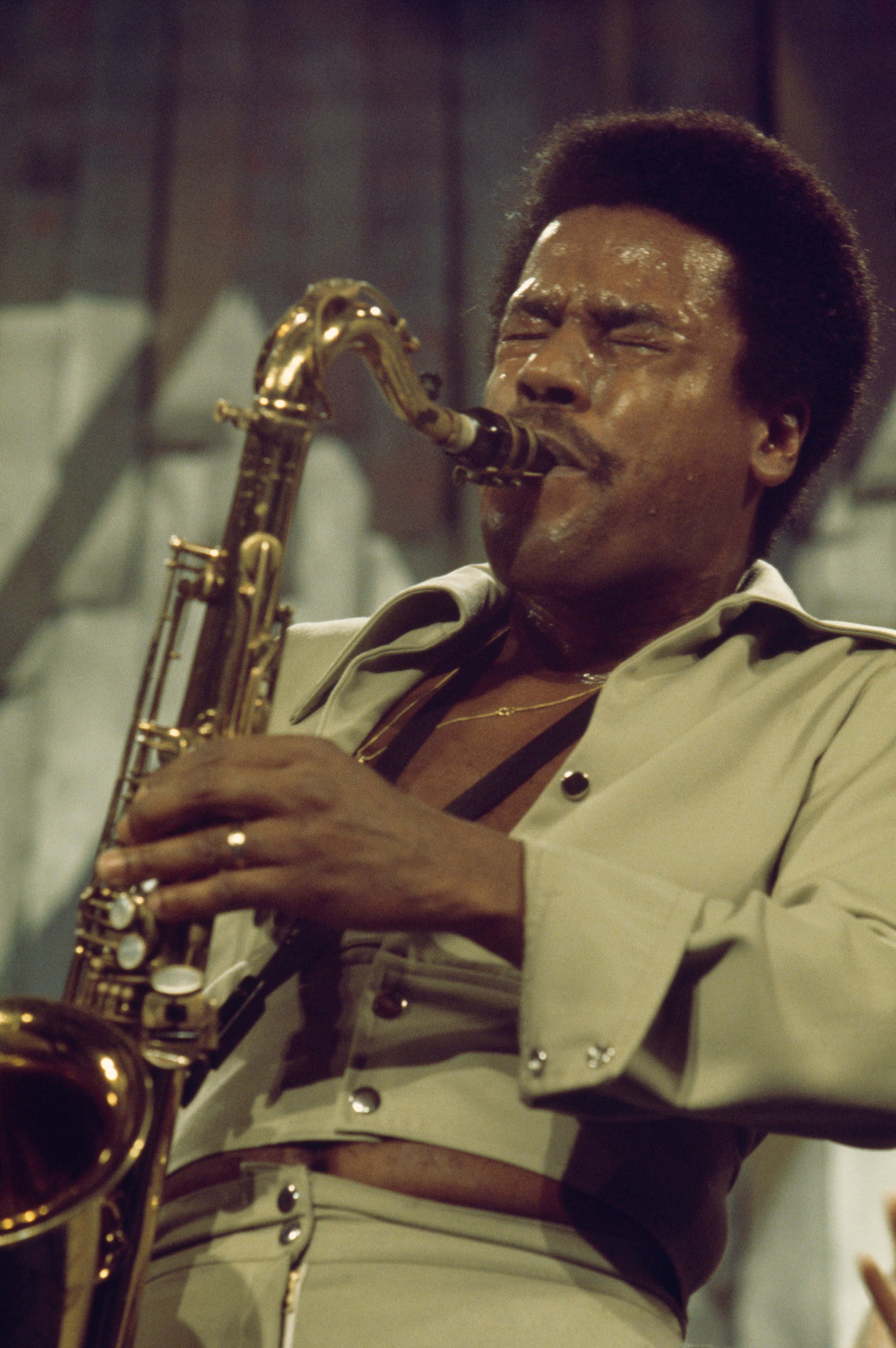 Wayne Shorter 桌布 壁紙 — 一位充滿熱情的爵士音樂家在溫暖燈光的舞台上閉著眼睛演奏金色色士風。