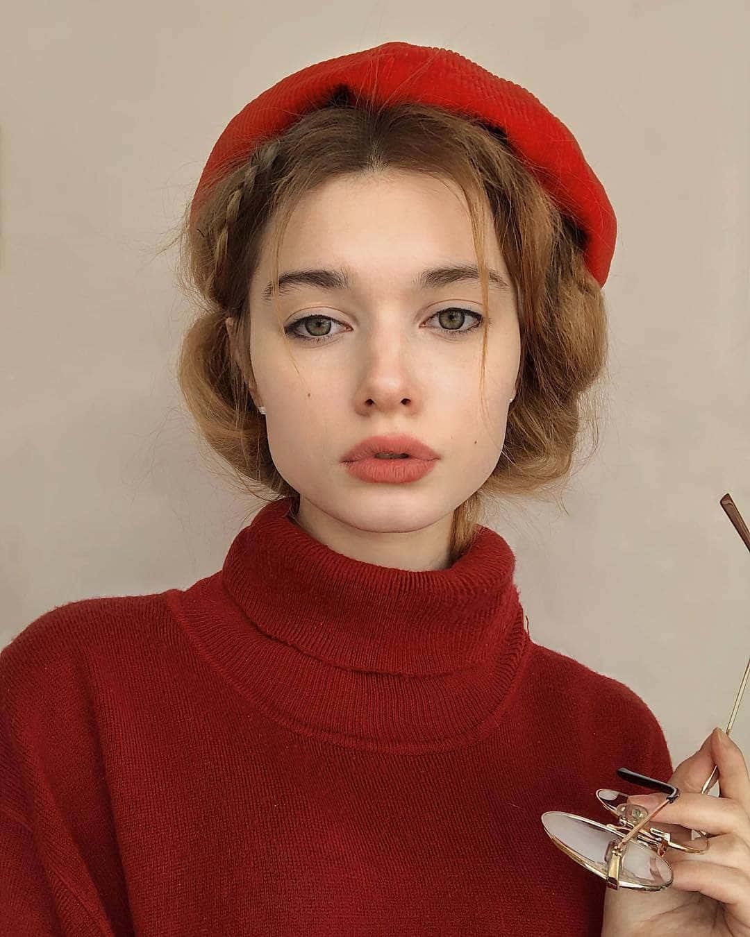 戴紅色貝雷帽和毛衣的女性在工作室肖像中拿著眼鏡。