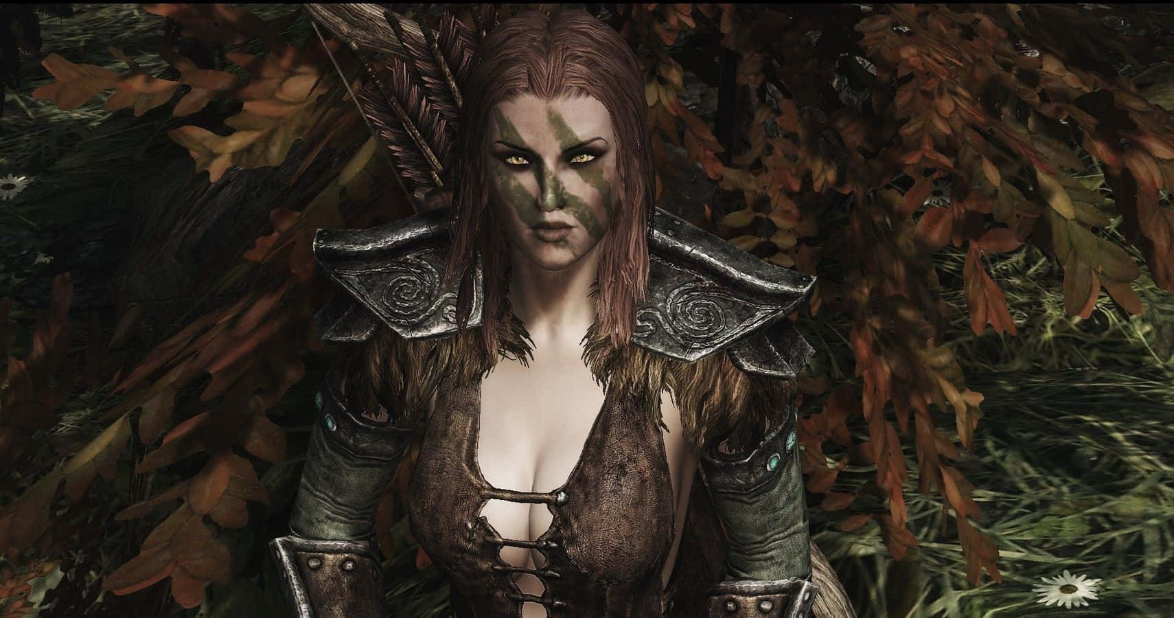 Aela The Huntress 桌布 壁紙 — 一位兇猛的女戰士，臉上塗著綠色顏料，身穿羽毛盔甲，站在茂密森林的秋葉中。