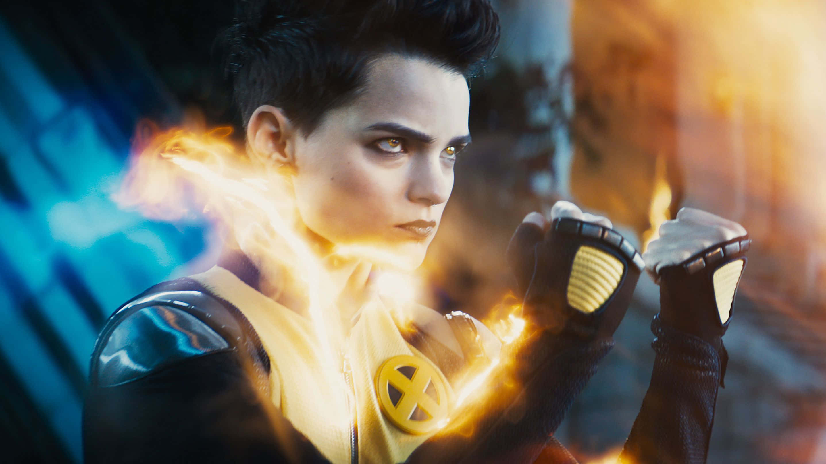 Negasonic Teenage Warhead 桌布 壁紙 — 一位兇猛的女超級英雄，留著黑色短髮，擁有發光的黃色眼睛，在模糊的藍色和橙色背景前從拳頭釋放出火焰能量。
