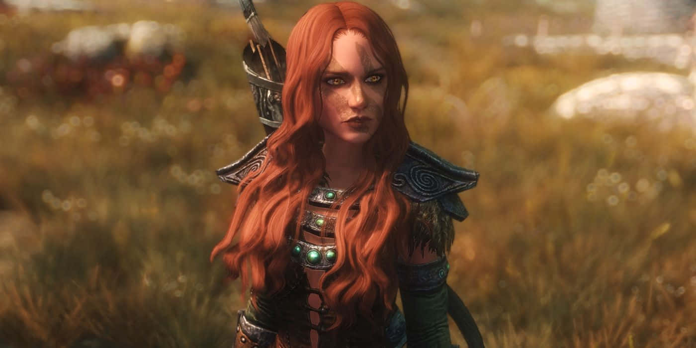 Aela The Huntress 桌布 壁紙 — 一位兇猛的紅髮女戰士身穿華麗盔甲，背著弓，站在陽光明媚的草地上。