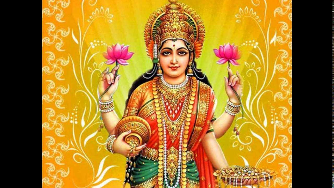 Lakshmi 桌布 壁紙 — 一位光彩照人的印度教女神，佩戴金色珠寶，身穿紅綠服飾，在發光的黃色花卉背景前手持粉紅蓮花和一個碗。