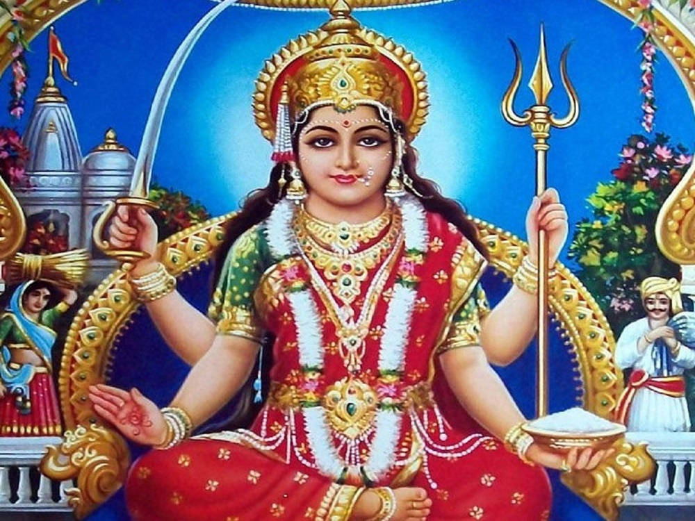 Goddess 桌布 壁紙 — 一位光彩照人的印度教女神，身著紅金服飾，威嚴地坐著，手持三叉戟和劍，背景是藍天、寺廟和花卉。