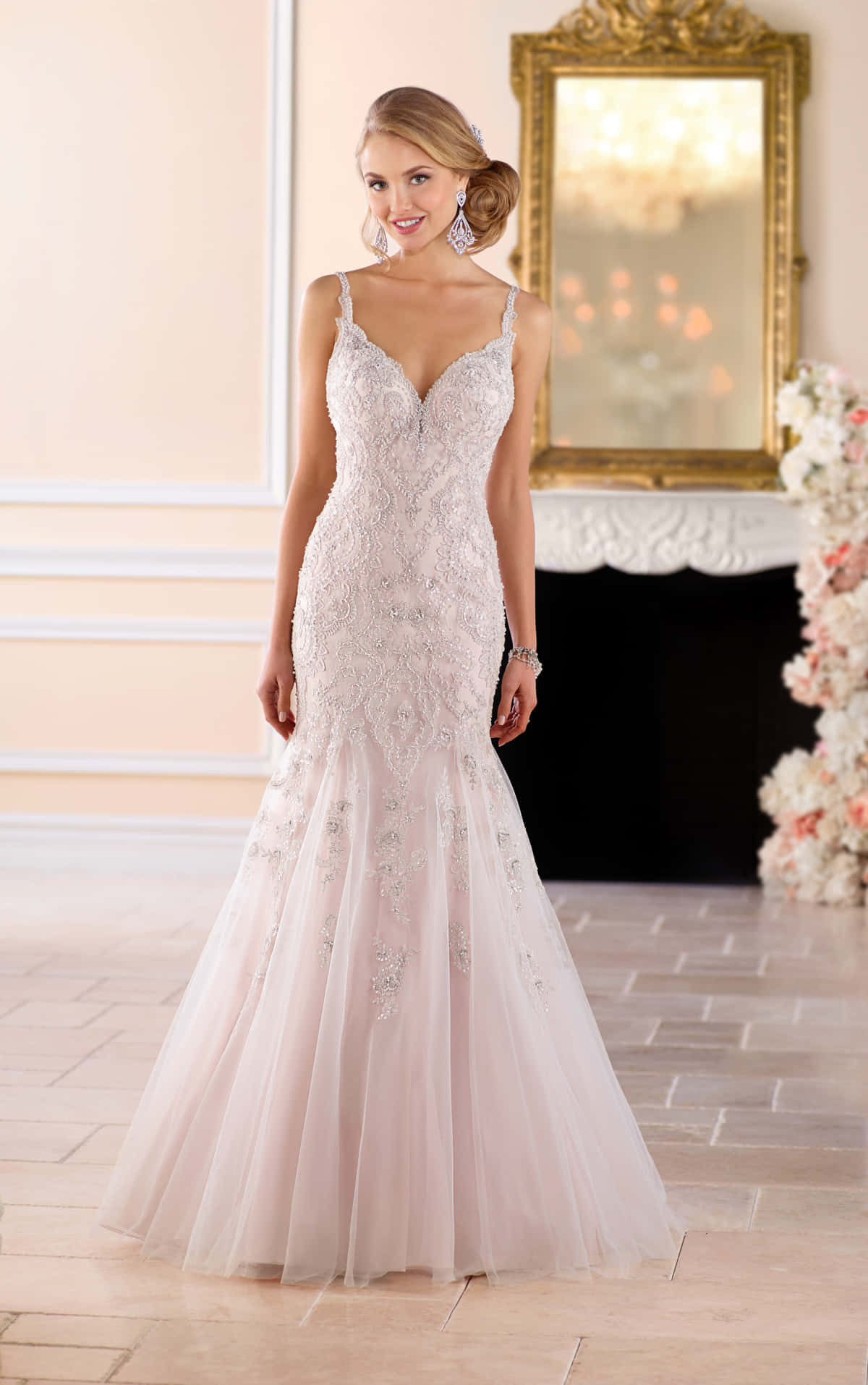 Wedding Dress 桌布 壁紙 — 一位光彩照人的新娘，身穿帶有精緻蕾絲和珠飾的淡粉紅色美人魚婚紗，優雅地站在一個帶有花卉佈置和華麗金色鏡子的典雅房間中。