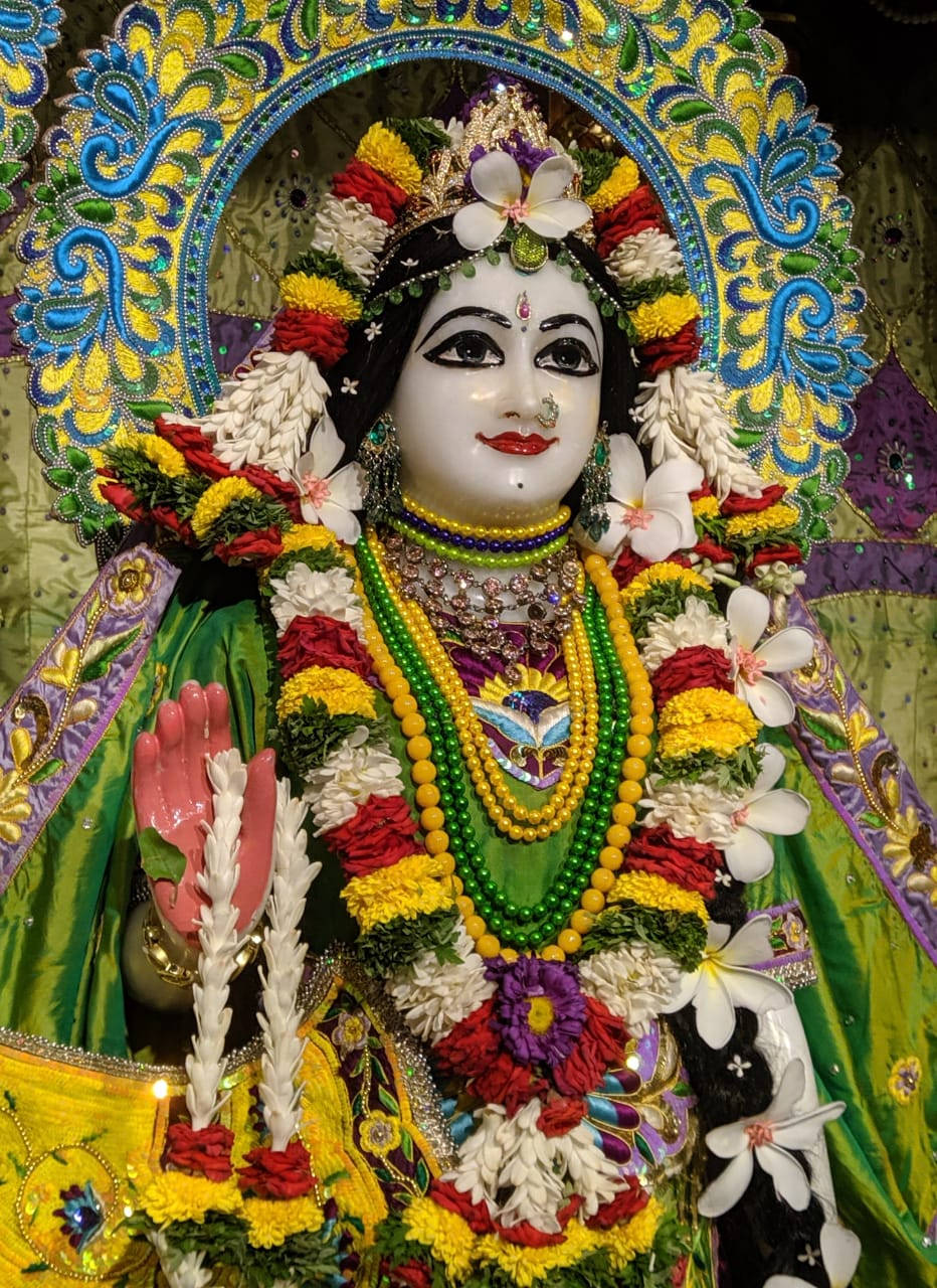 Hindu God 桌布 壁紙 — 一位光彩照人的神祇，在鑲滿寶石的拱門下，裝飾著鮮豔的花環和精緻的珠寶。