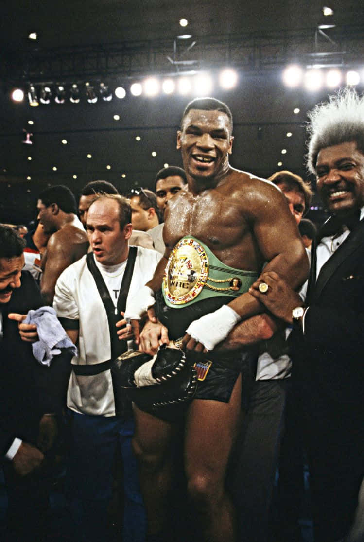 mike tyson 桌布 壁紙 — 一位勝利的拳擊手在明亮的競技場燈光下，被慶祝的人群包圍，手持冠軍腰帶，滿臉喜悅。