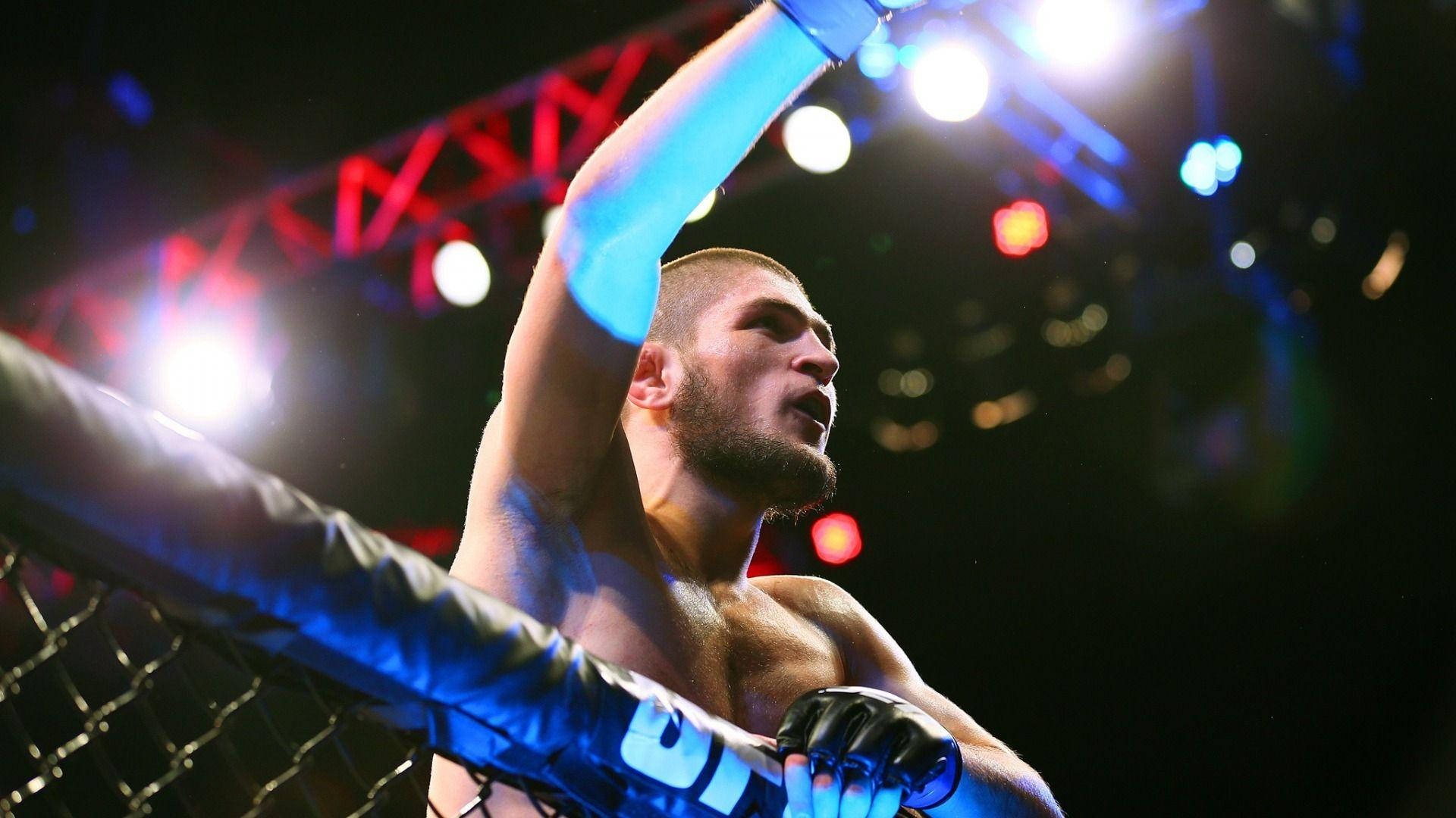 UFC 桌布 壁紙 — 一位勝利的混合武術家喺明亮嘅八角籠內高舉手臂慶祝勝利。