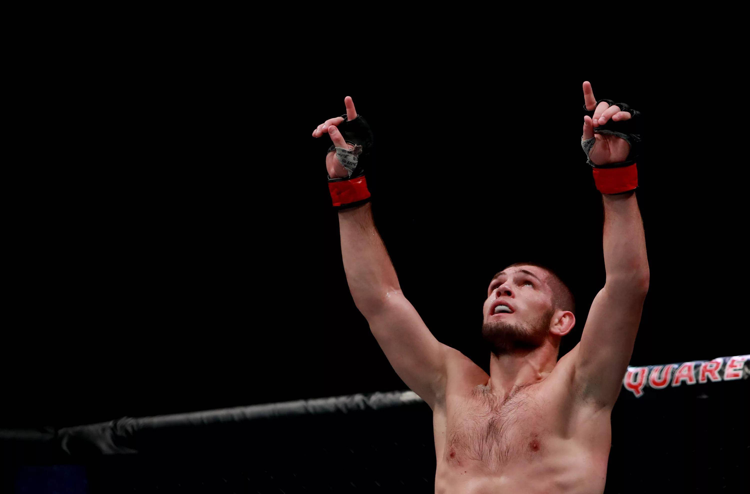 UFC 桌布 壁紙 — 一位勝利的混合武術家在昏暗的黑色背景八角籠中高舉雙臂慶祝勝利。