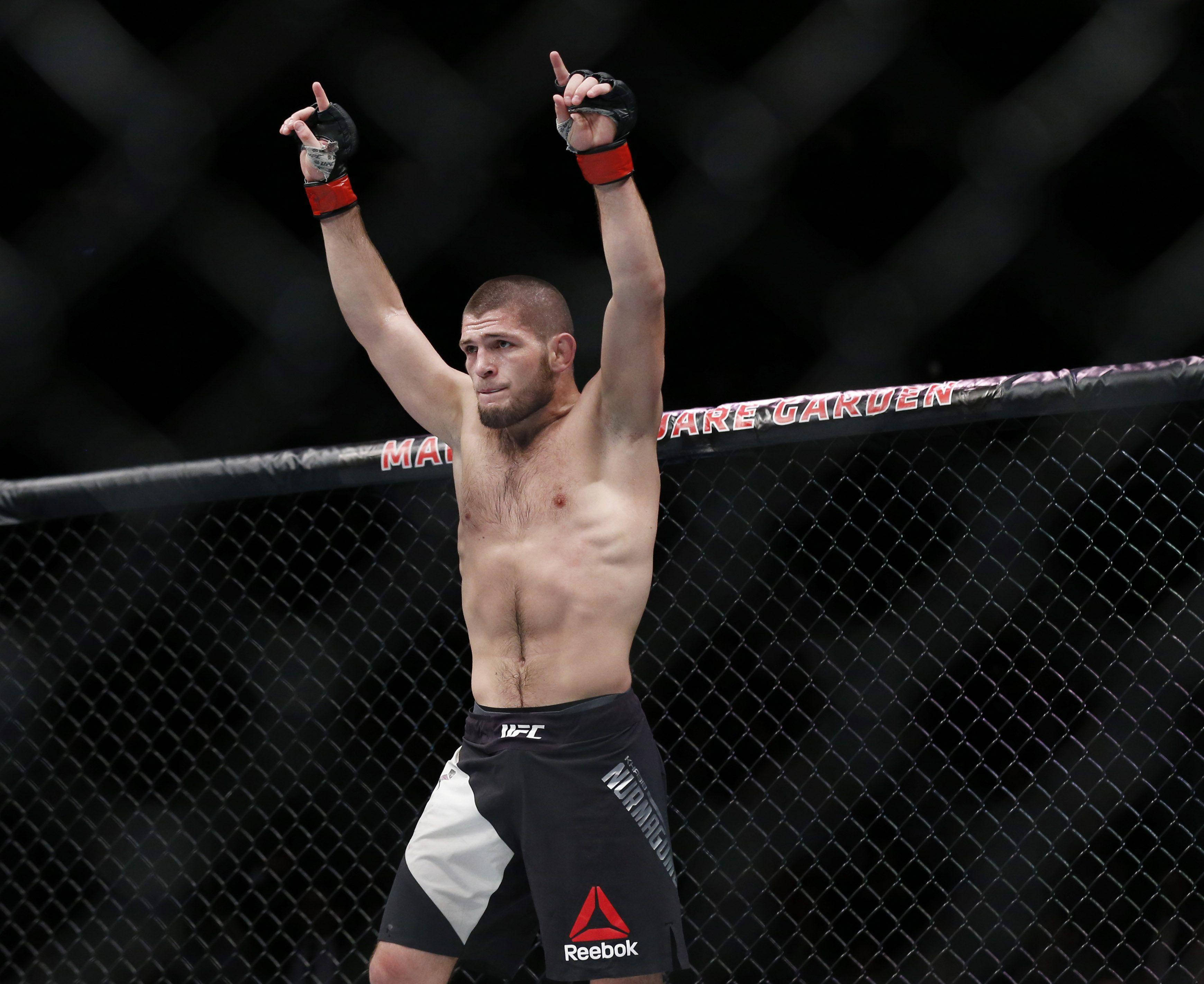 UFC 桌布 壁紙 — 一位勝利的混合武術選手在昏暗的八角籠內高舉雙臂慶祝勝利。