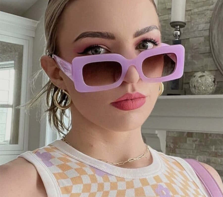 Purple Sunglasses 桌布 壁紙 — 一位化著大膽妝容的女性在室內壁爐附近戴著超大薰衣草色太陽眼鏡。
