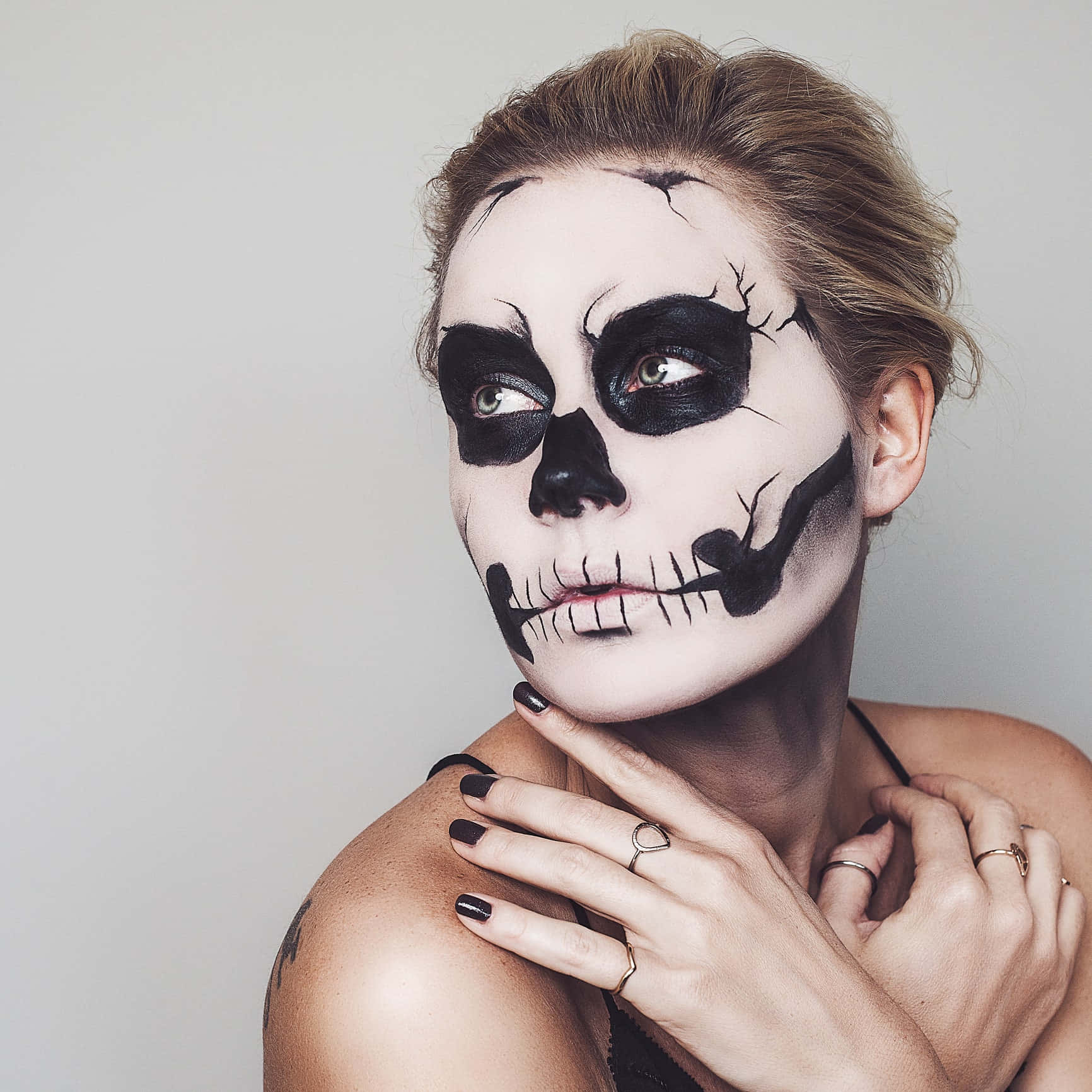 Halloween Face Paint 桌布 壁紙 — 一位化著精緻黑白骷髏妝容的女性，在純灰色背景上向上凝視。