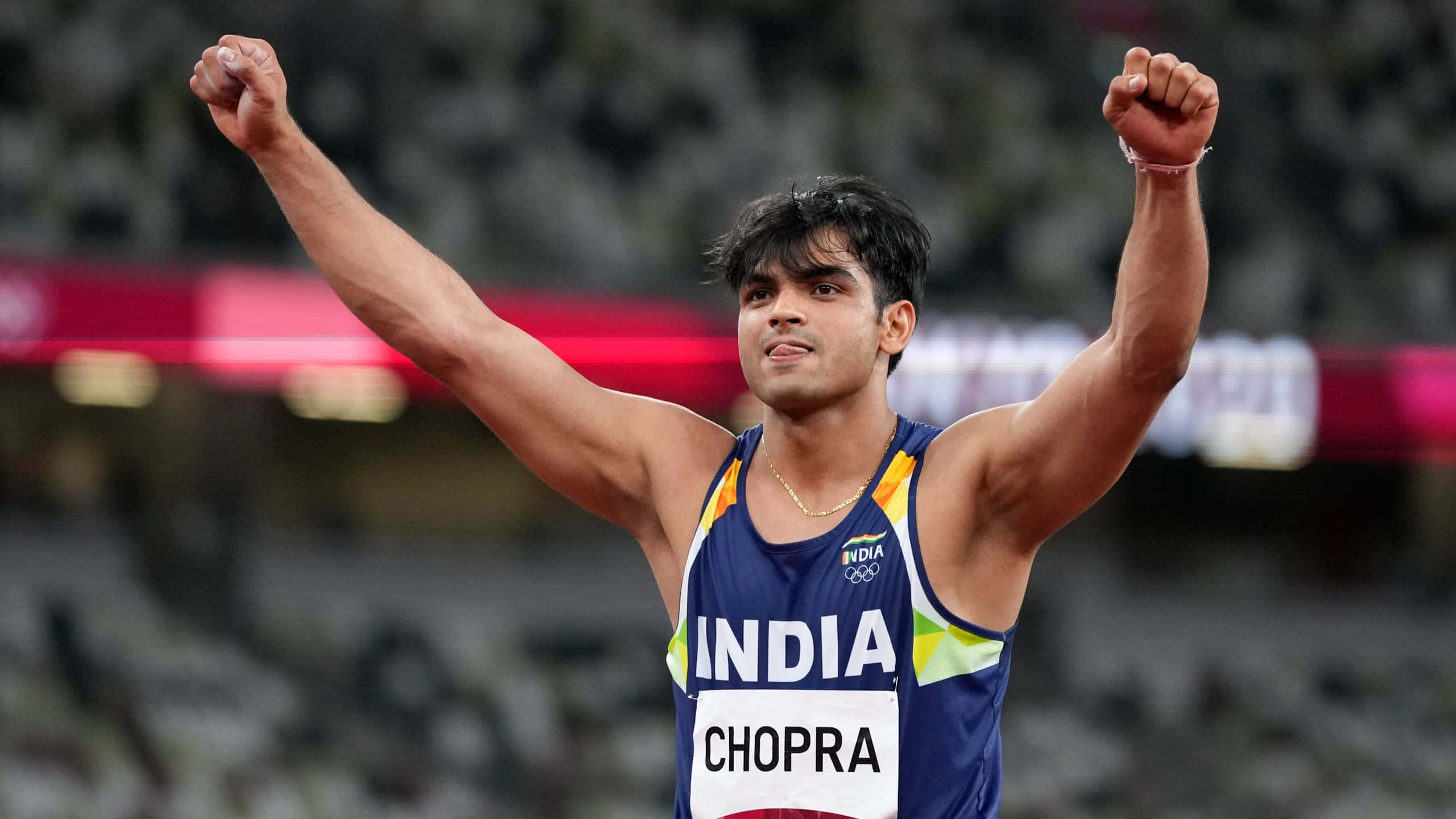 Neeraj Chopra 桌布 壁紙 — 一位印度標槍運動員在明亮的燈光下於體育館內舉起拳頭慶祝勝利。