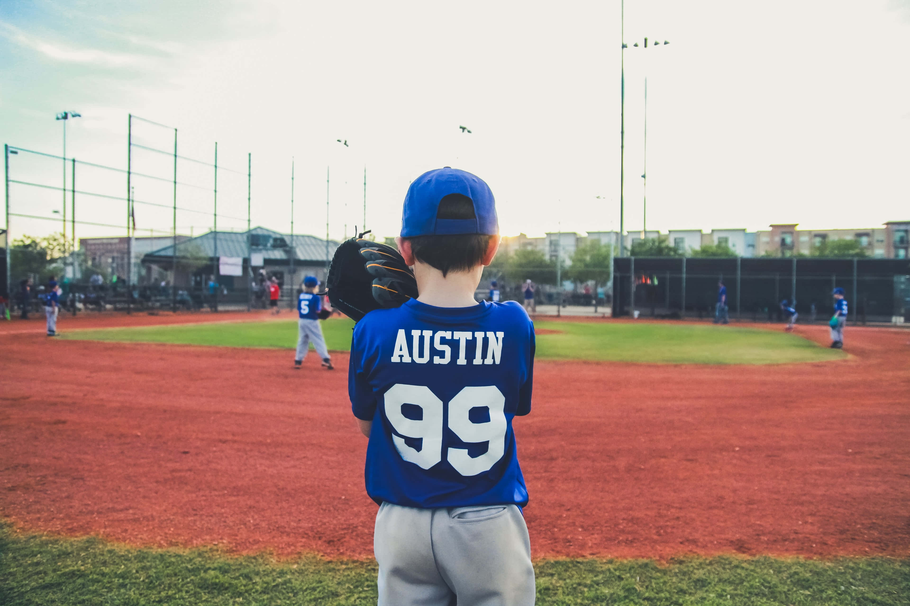 Little League Baseball 桌布 壁紙 — 一位名叫奧斯汀的年輕棒球選手穿著99號球衣，站在陽光明媚的球場上，手持手套。