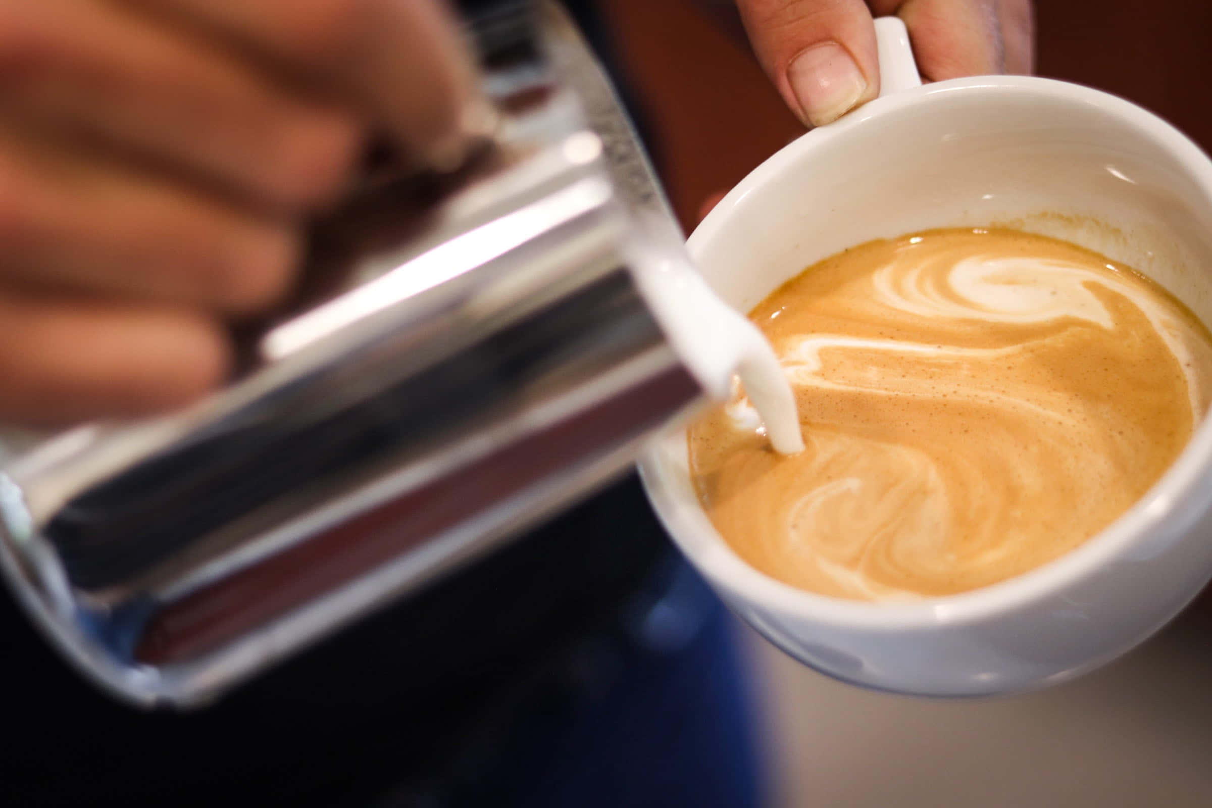 Milk And Coffee 桌布 壁紙 — 一位咖啡師將蒸氣牛奶倒入裝有濃縮咖啡的白色杯子中，創造出精緻的拉花漩渦。