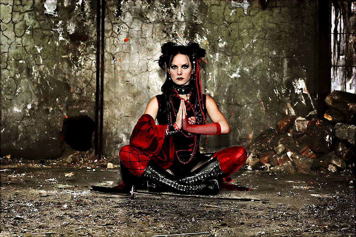 Gothic Fashion 桌布 壁紙 — 一位哥德式女性身穿紅黑服飾，在一個牆壁破裂、佈滿瓦礫的廢棄工業空間中盤腿而坐。