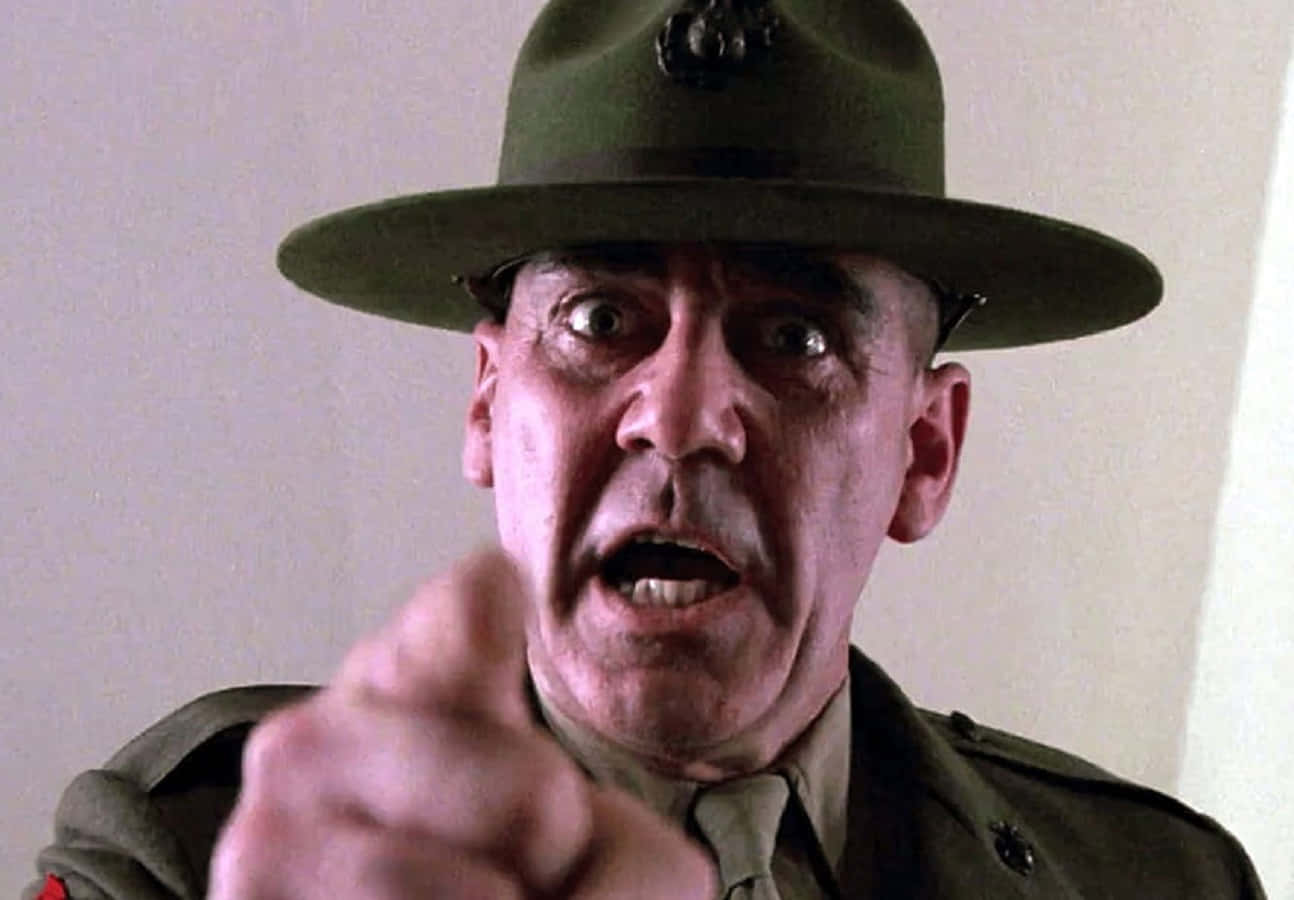 R. Lee Ermey 桌布 壁紙 — 一位嚴厲的海軍陸戰隊教官，身穿綠色制服和帽子，睜大眼睛、張開嘴巴，憤怒地直接指向觀眾。