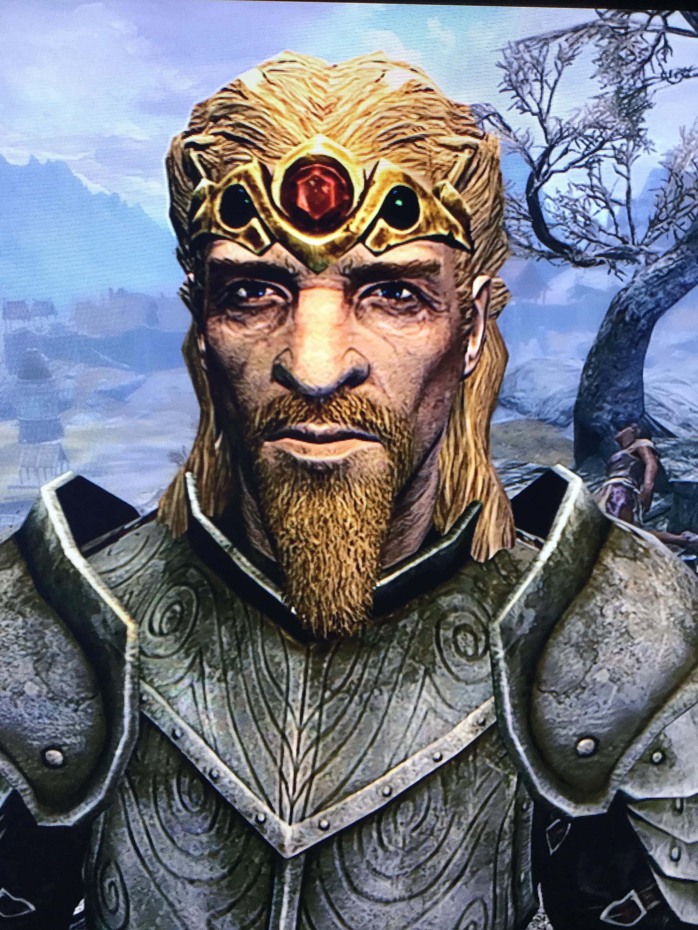 Jarl Balgruuf 桌布 壁紙 — 一位嚴肅的裝甲戰士，戴著金色王冠和紅色寶石，在霧氣繚繞的山景背景下凝視前方。