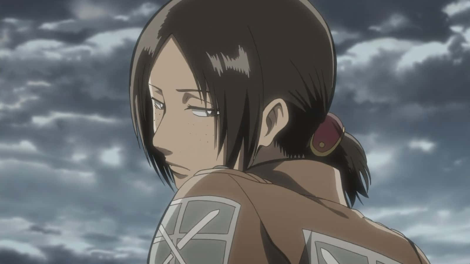 Ymir 桌布 壁紙 — 一位堅定的動畫士兵，身穿帶有徽章的棕色制服，凝視著多雲的灰色天空。